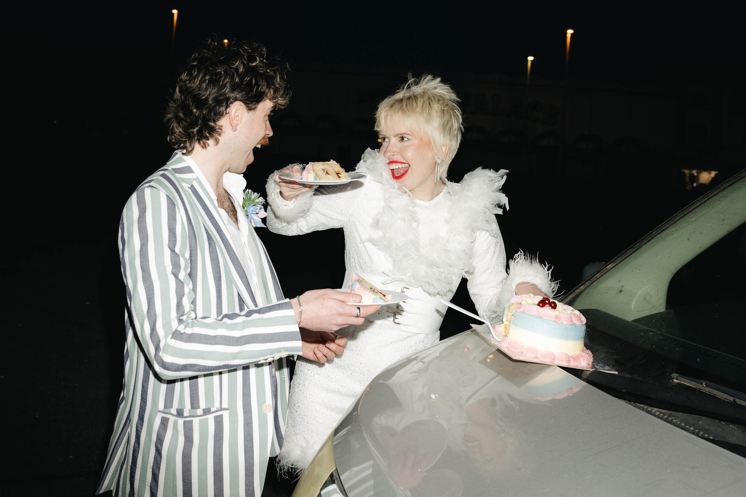Couple eating vintage-inspired wedding cake on the hood of their camper van