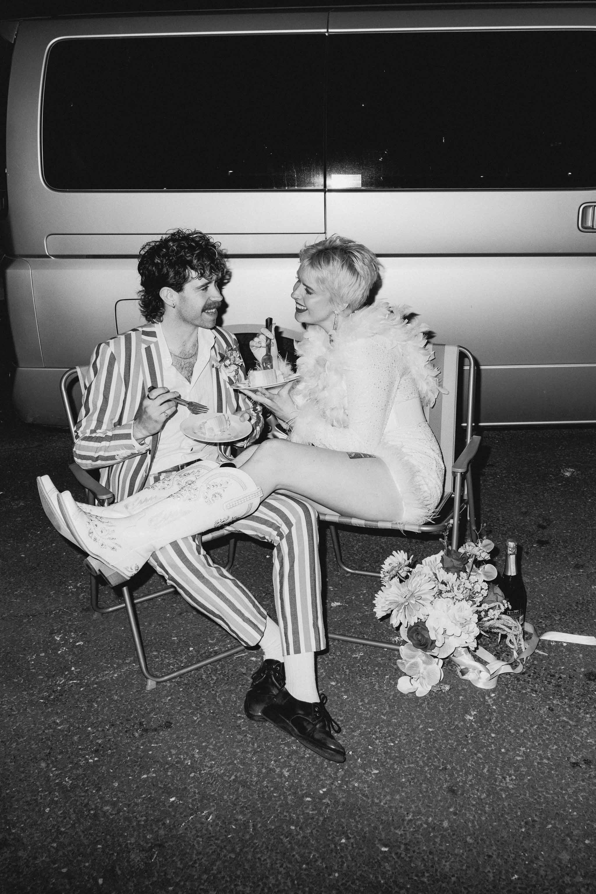 Couple eating vintage-inspired wedding cake sat in front of their camper van