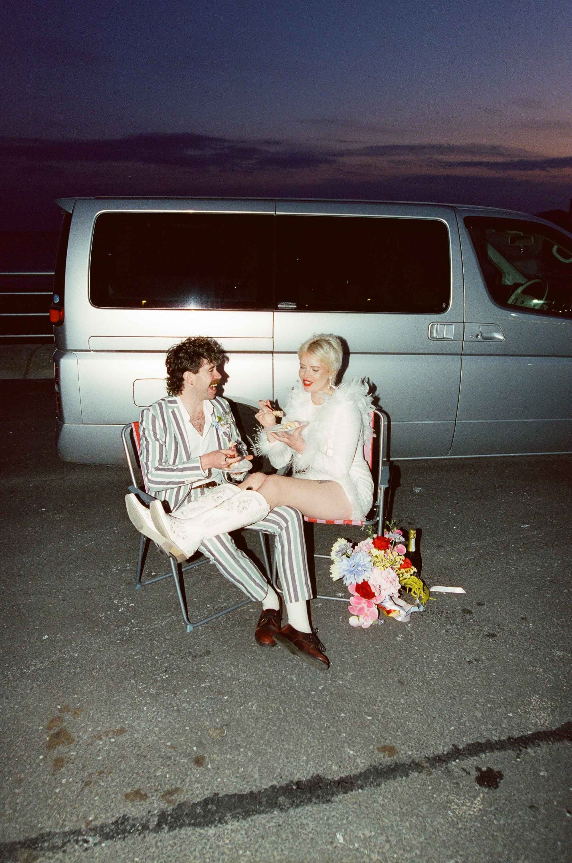 Couple eating vintage-inspired wedding cake on the hood of their camper van, captured on 35mm film
