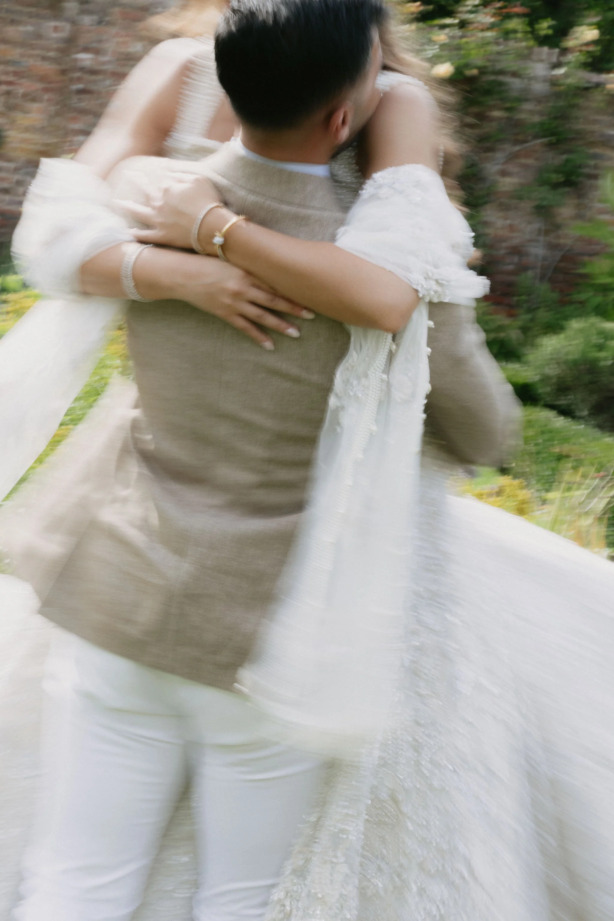  Blurry image of a couple embracing and spinning in wedding outfits. 