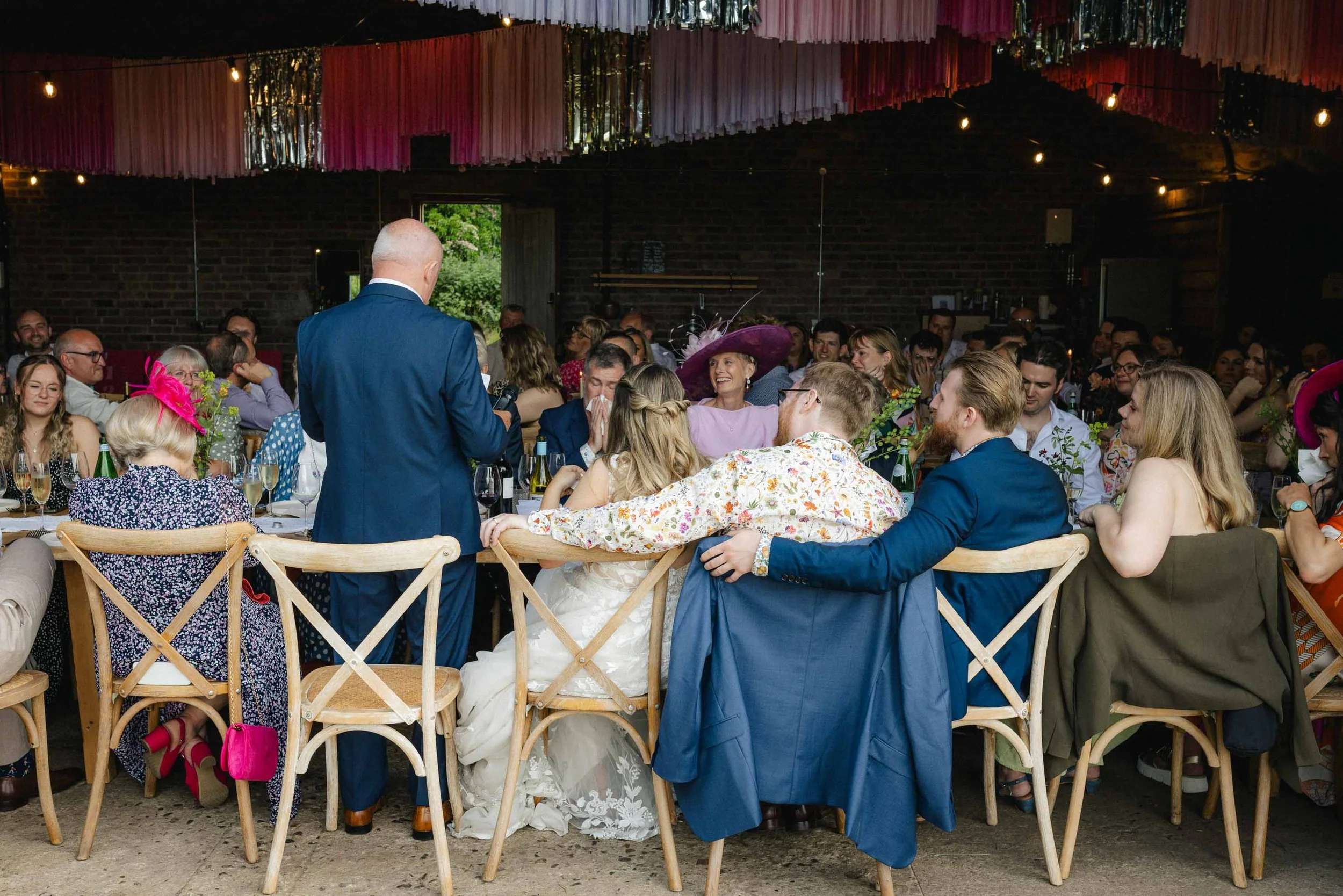  Wedding couple and groomsman sitting with their arms round each other during speeches. 