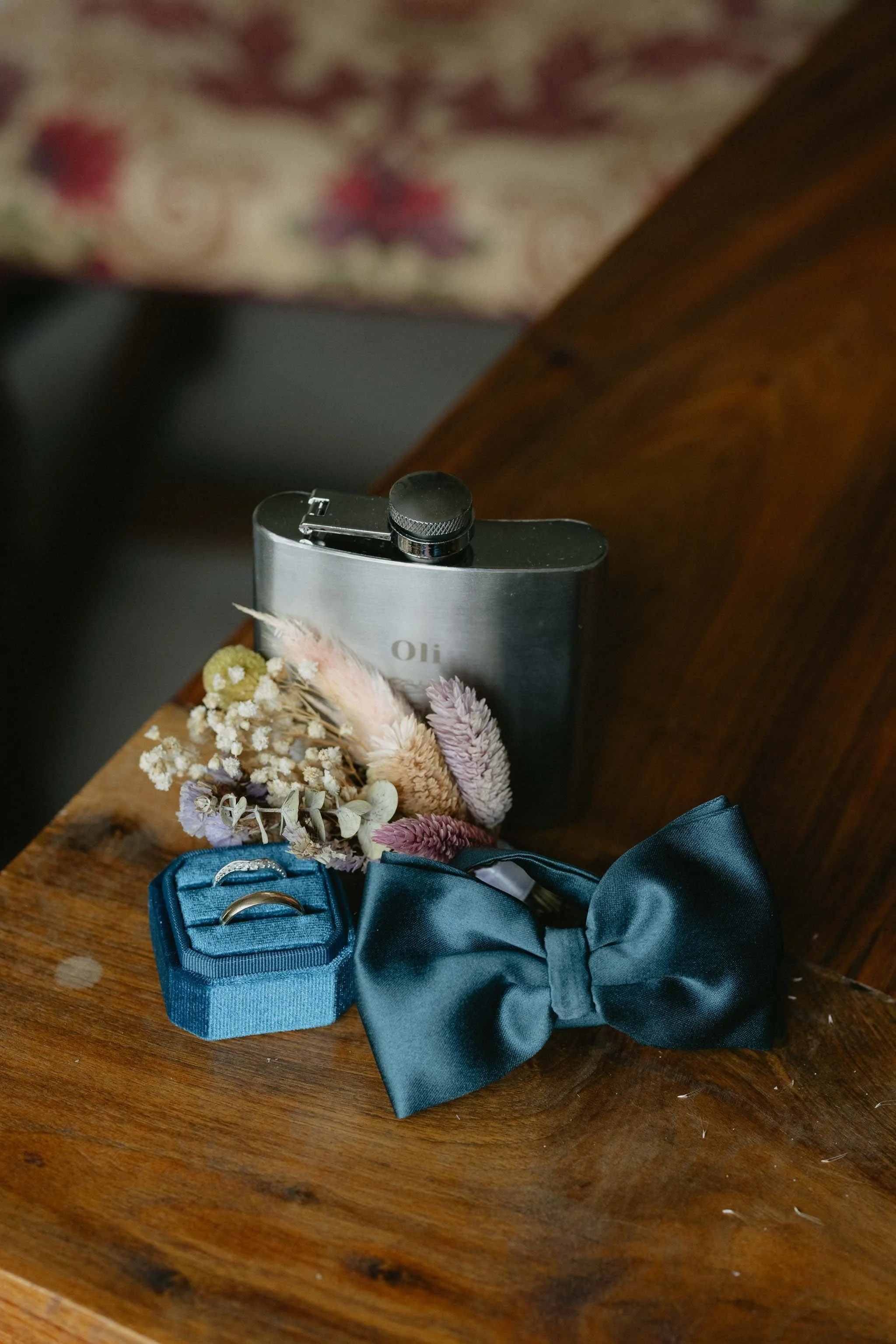 Wedding day details featuring rings, a flask and button hole. 