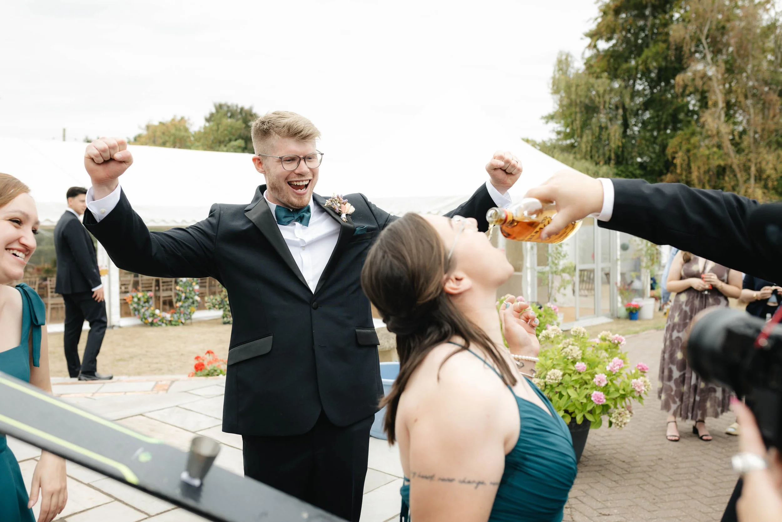  Groom cheering as a drink is pouted into a guests mouth during a wedding reception at home in Worcester. 