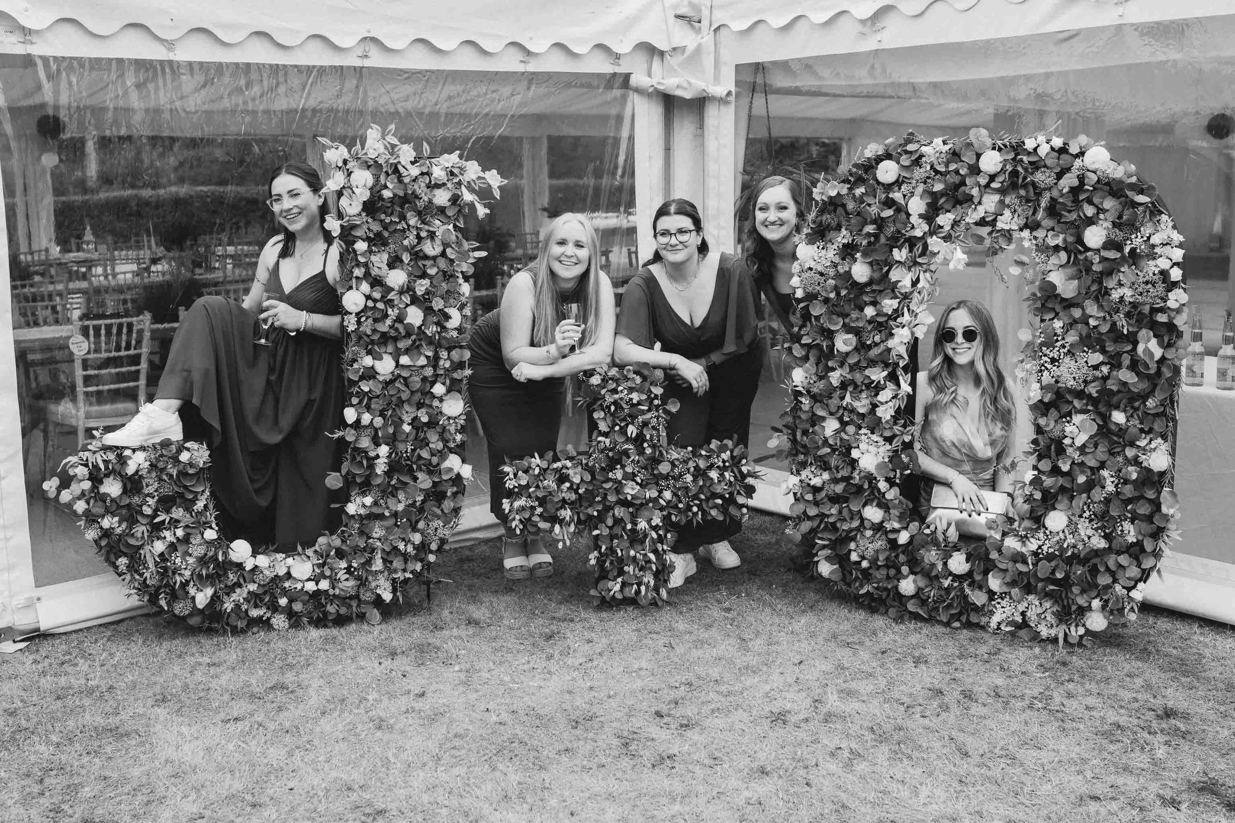  Wedding guests posing by a floral installation at a backyard wedding reception in Worcester. 