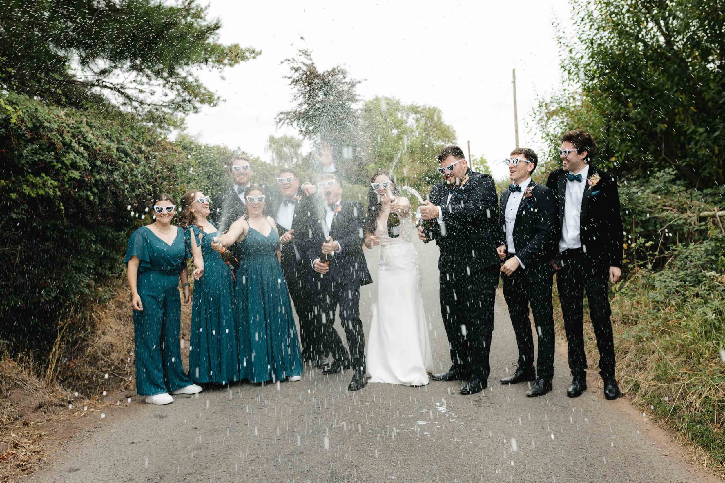  Jess + Oli spraying champagne with bridal party at Worcester wedding marquee reception. 