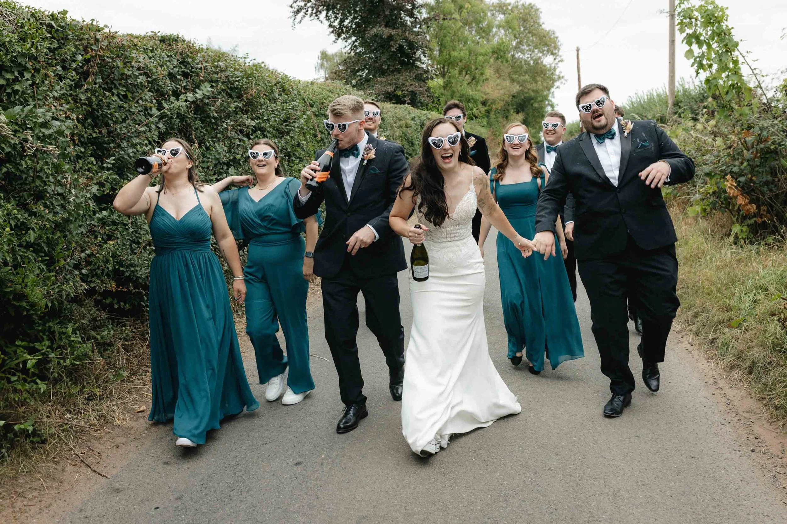  Candid moment of Jess + Oli enjoying champagne spray with bridal party at their marquee wedding in Worcester.   
