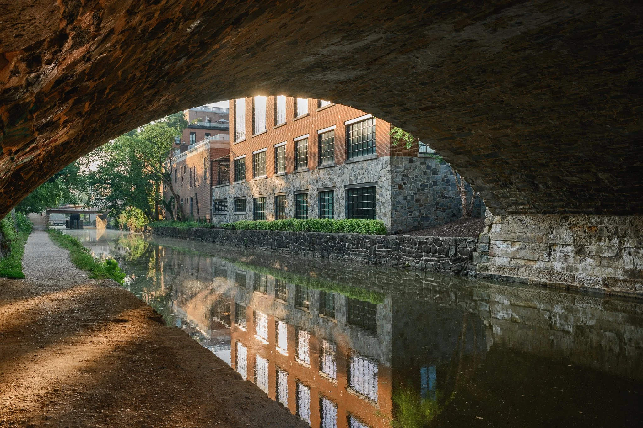 View of the C&O Canal towpath and buildings in Georgetown from under a bridge.