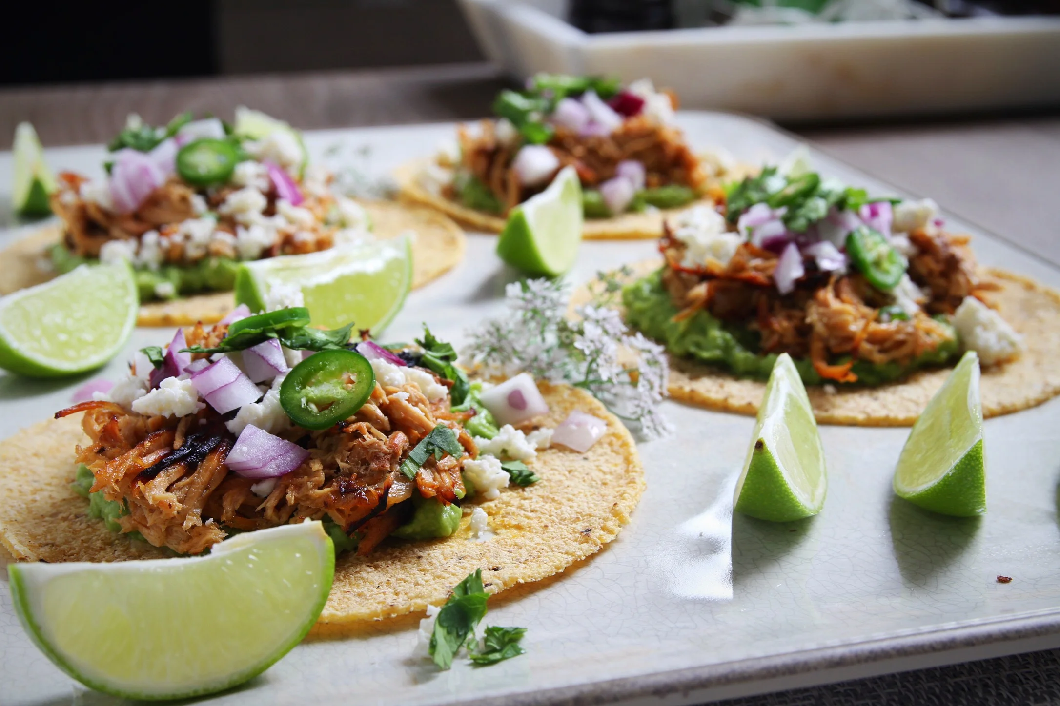 Carnitas tacos with all of the trimmings: guacamole, queso fresco, red onion, Serrano peppers.