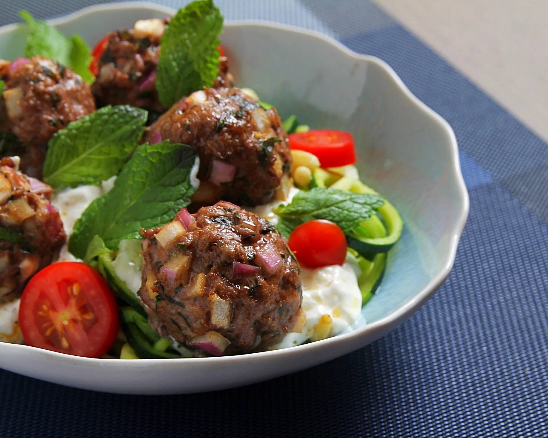 Greek lamb meatballs with zucchini noodles and lemon-yogurt dipping sauce. Fresh mint and grape tomatoes.  