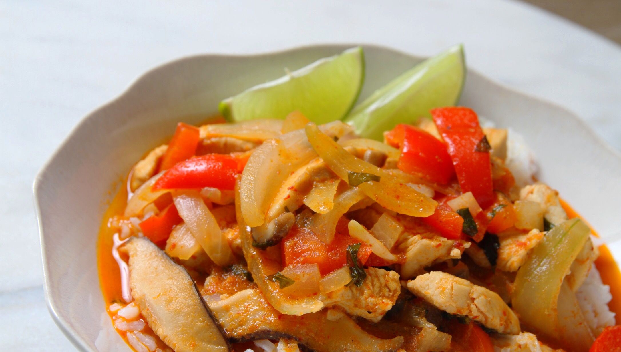 Red Coconut Curry Chicken served over Jasmine rice. Lime wedge garnish.
