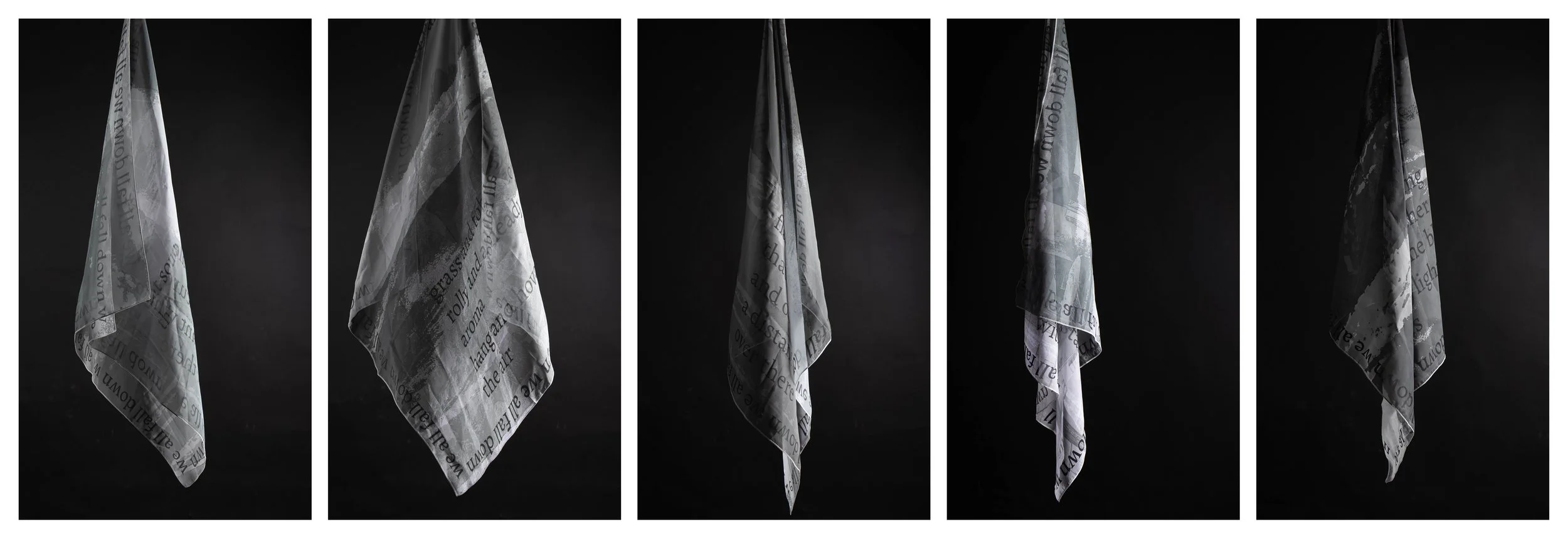 Five scarves hang on a black background. They are black, grey and white and contain words.