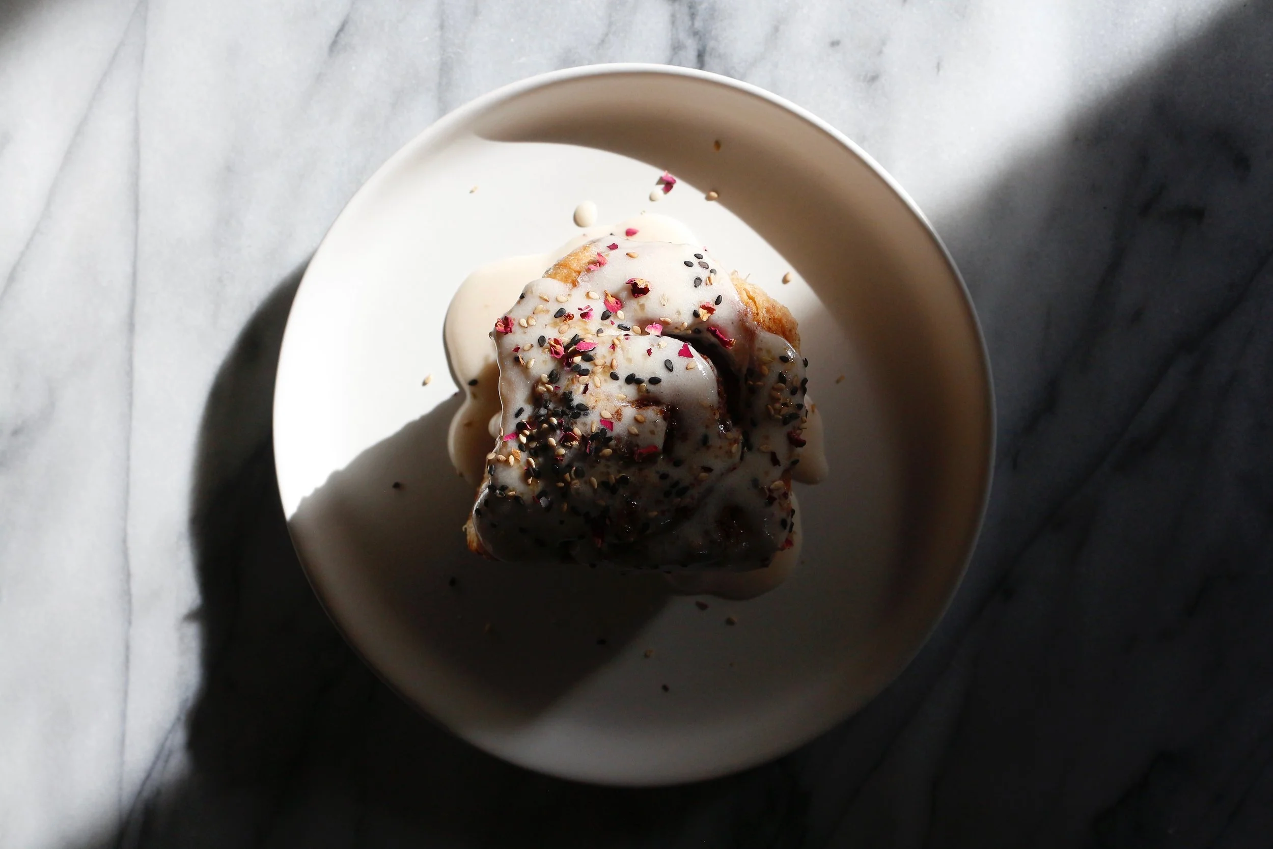Ordinary cinnamon rolls these are not. Nutty, rich tahini helps to keep these rolls from being overly sweet, and a rose-infused milk brings floral notes to the creamy frosting. The slight tang from sourdough starter adds depth and balances sweet and savory flavors. Topped with a blend of toasted black and white sesame seeds, coarse sugar, crushed rose petals, and flaky salt for crunch and subtle reinforcement of the flavors present. Garnishes like this add visual interest and textural contrast, but they also offer the lucky eater a hint of what they're in for.