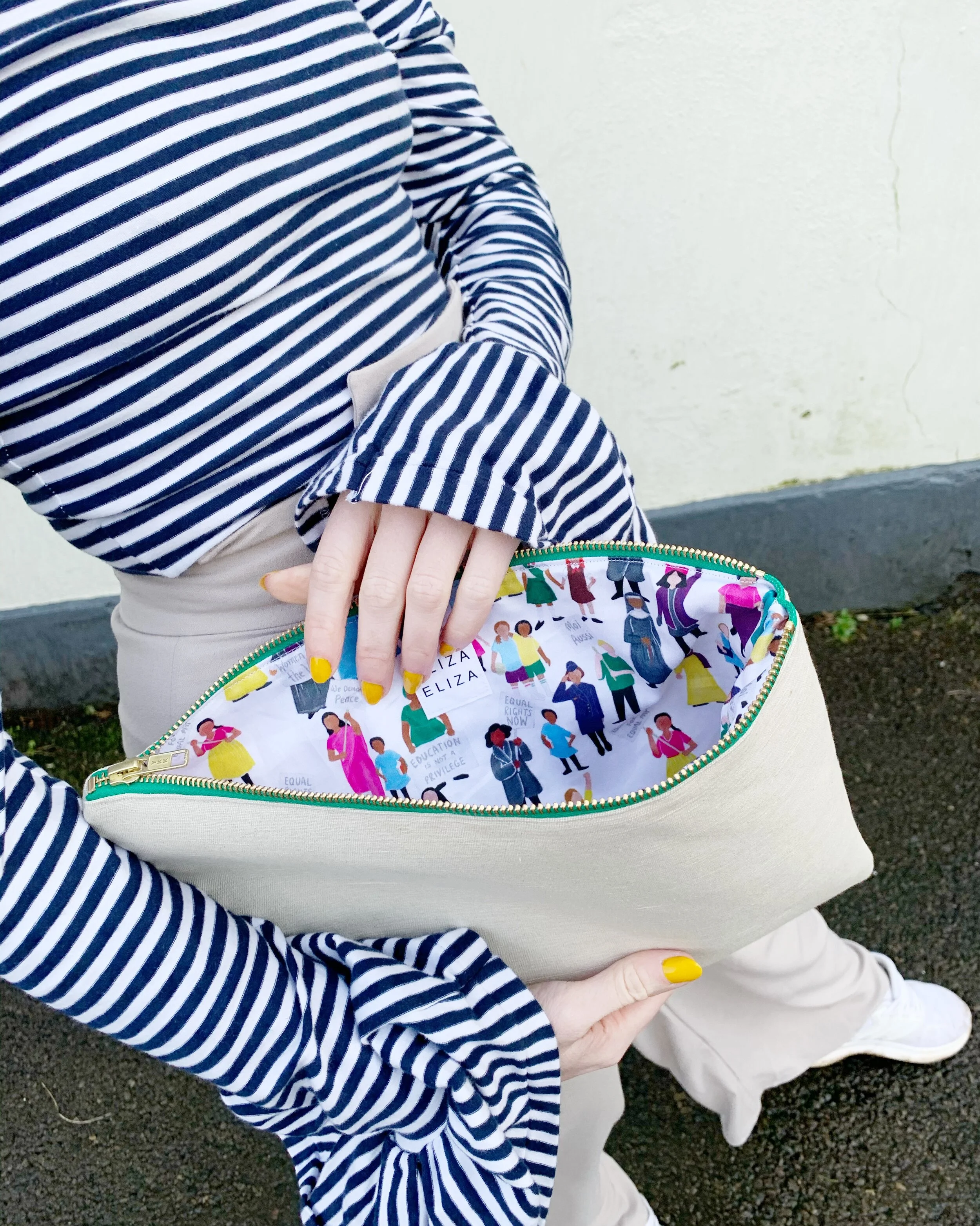 Person wearing long sleeve navy striped top holds open large equality collection hemp clutch bag