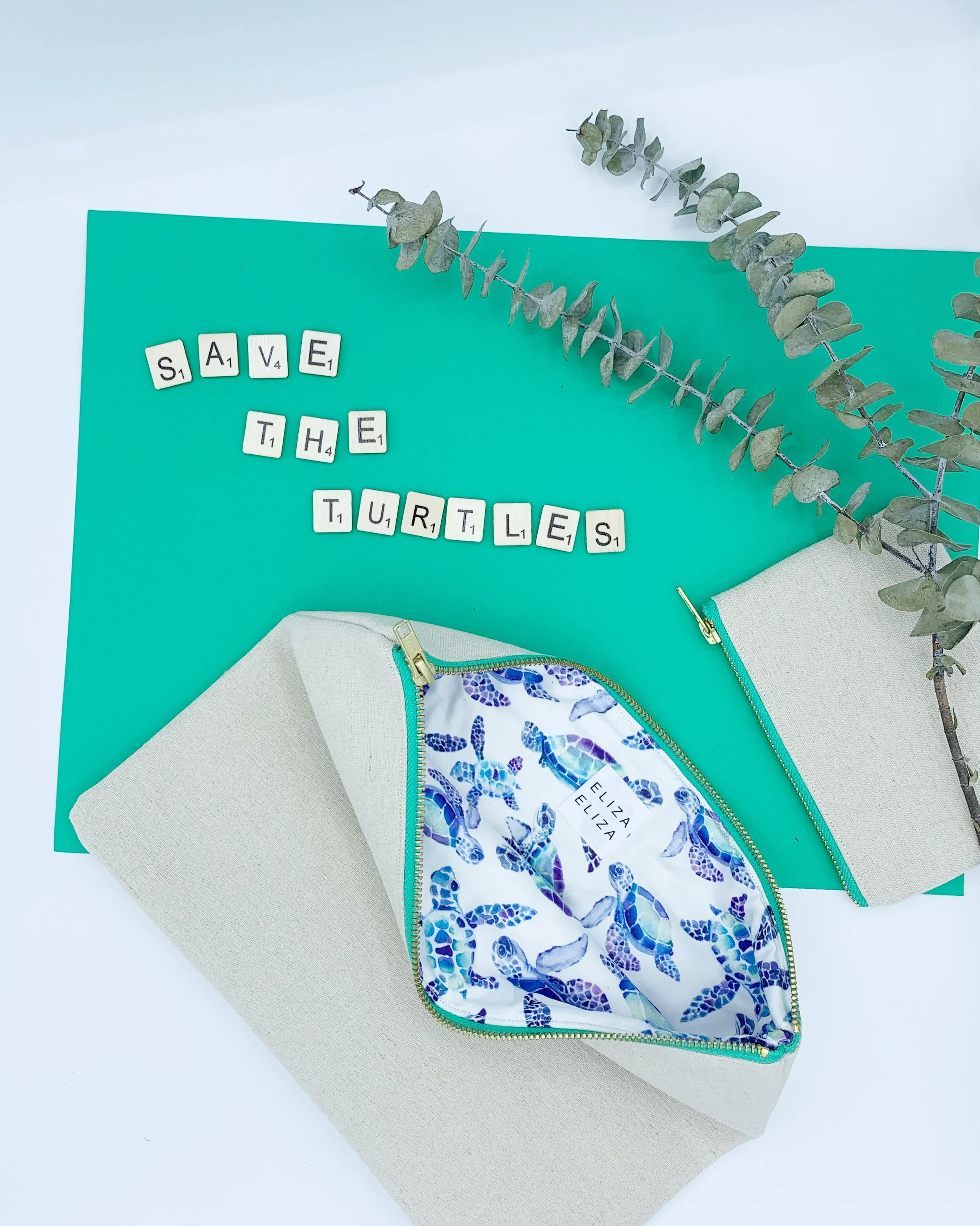 flat lay Turtle collection large clutch bag and purse sprig of eucalyptus scrabble letters spell out save the turtles