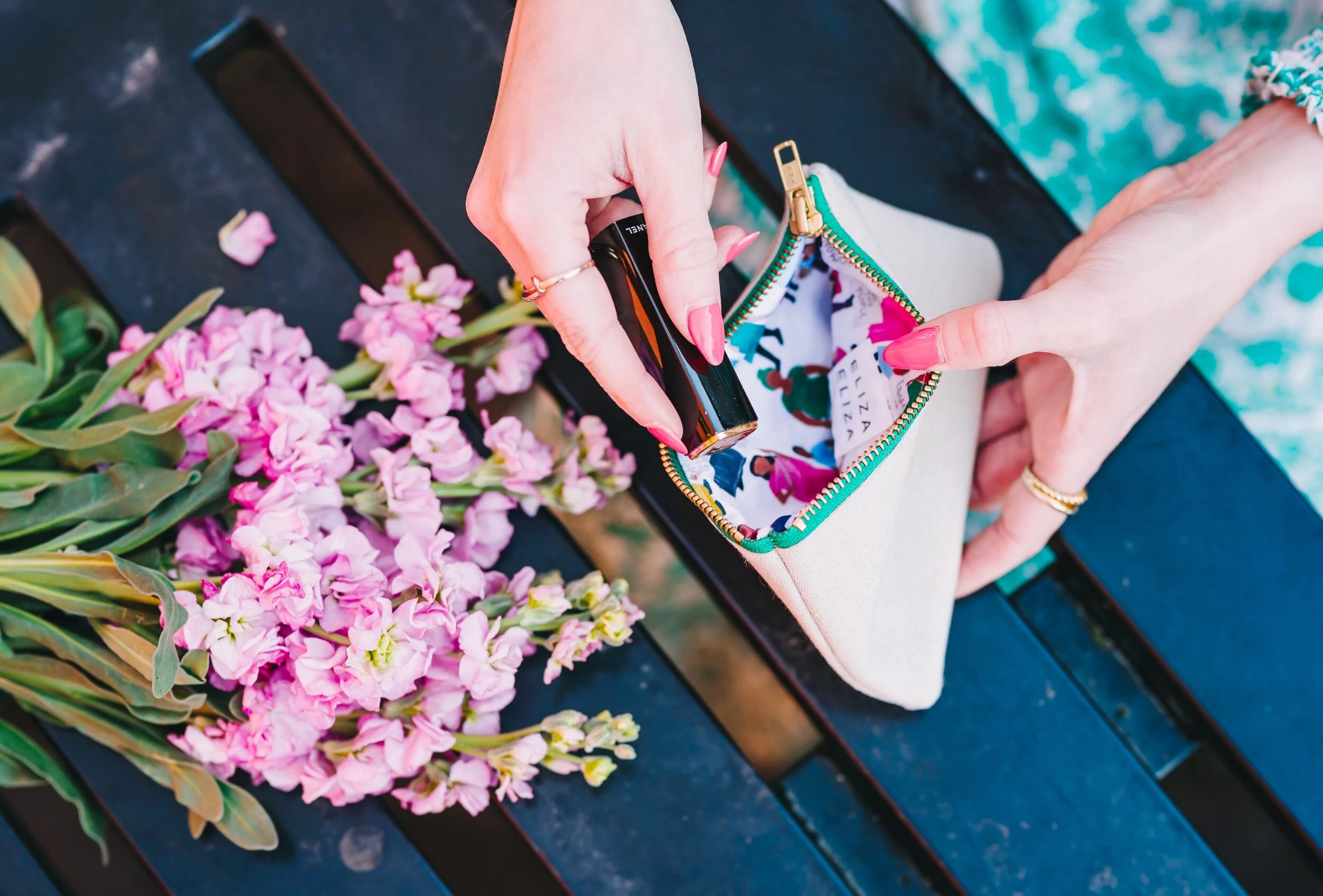 Equality Collection purse held open next to pink flowers, a hand with manicured pink nails takes out lipstick