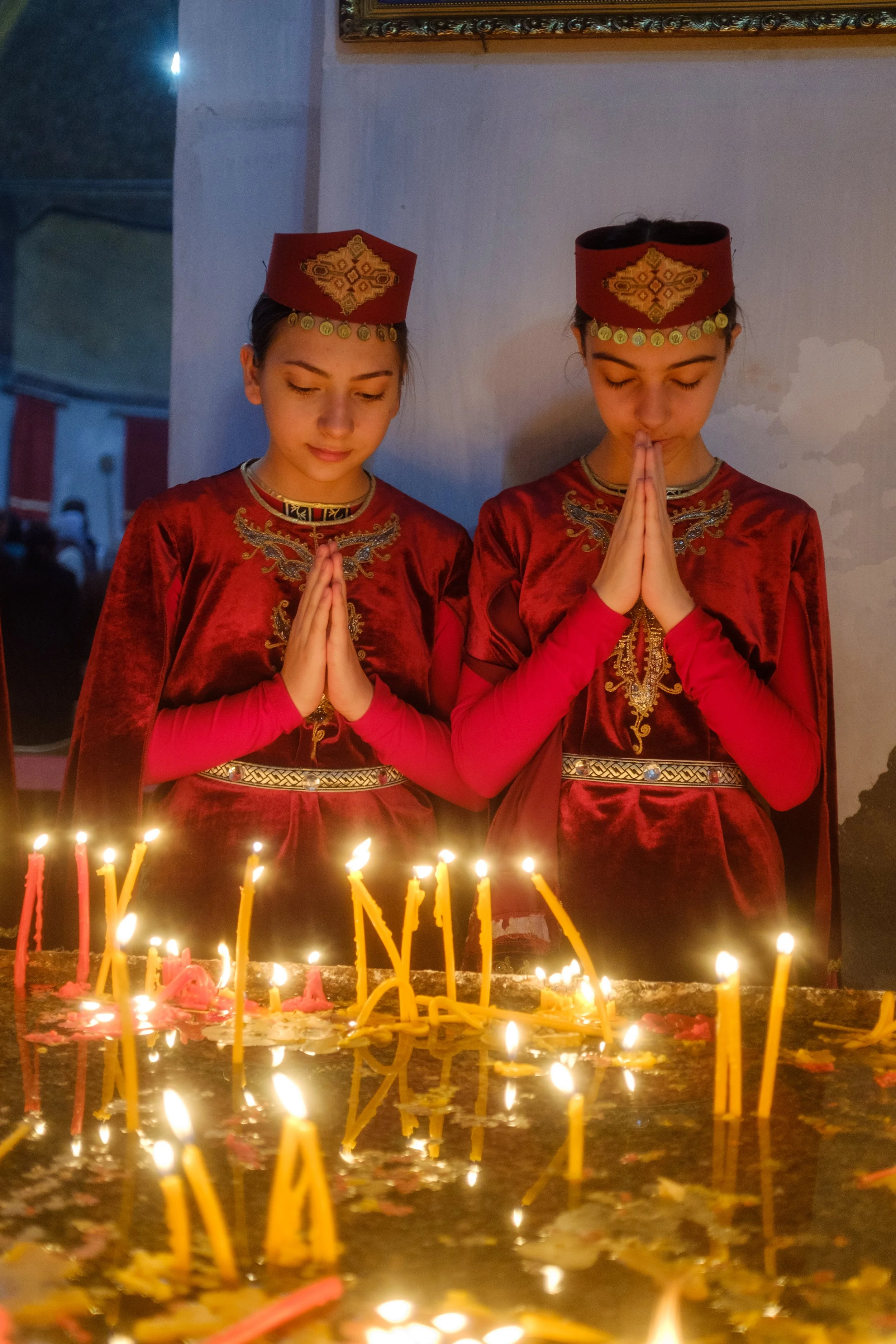  Two young Armenian women in traditional clothing pray after lighting candles. Holy Week in Armenia. From Palm Sunday to Easter, I traveled the country photographing the Armenian faith. Armenia, Gyumri, April 13, 2025.Deux jeunes armenienne en habits