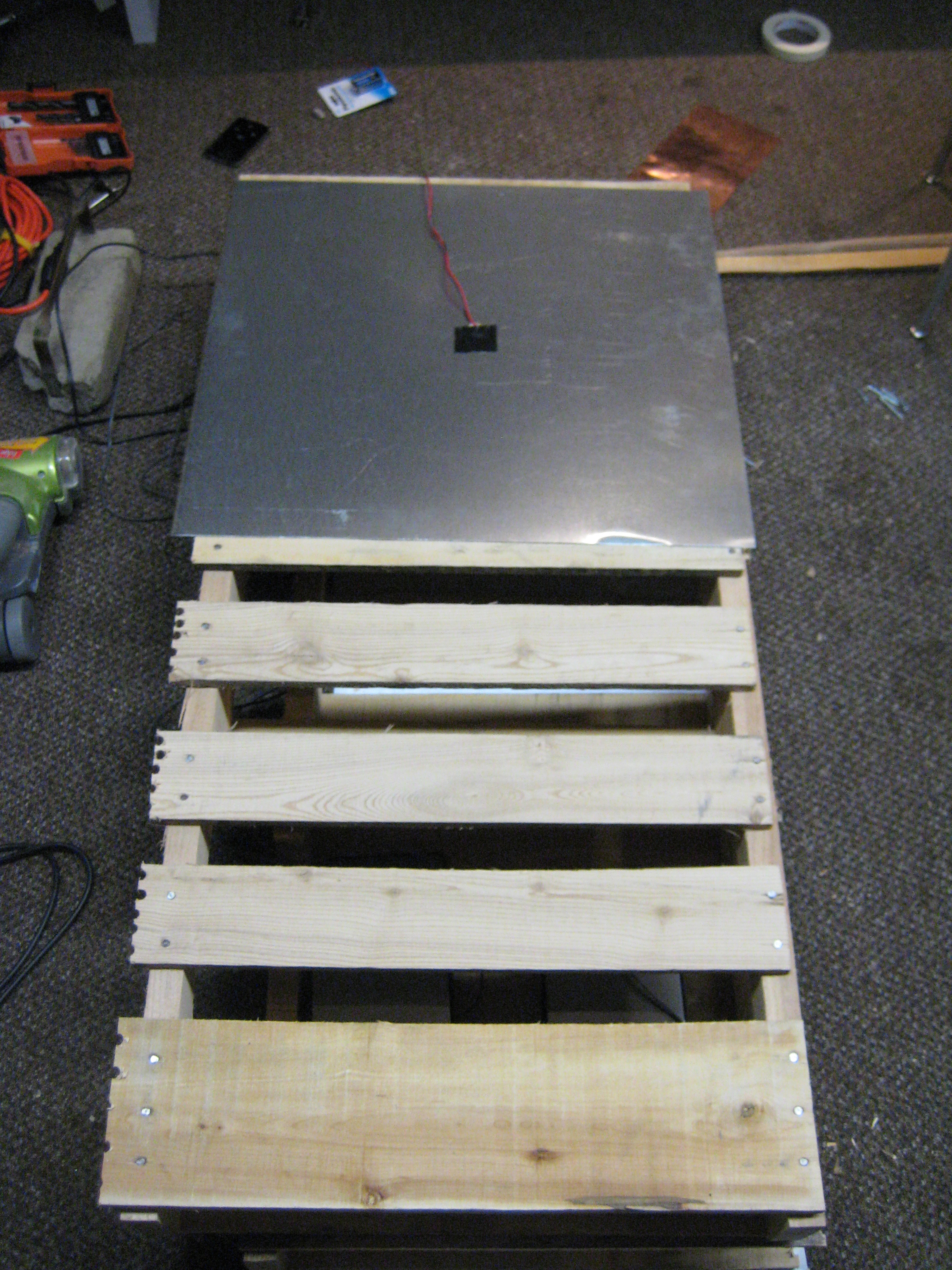The next phase of construction was to create a durable casing that could withstand violent movements from a dancer. My solution was to encase the electronics in a docking palette covered in sheet metal. The first step of this process was to cut a docking skid in half andplace one half of the skid on top of the other. I then attached a piezo microphone to the sheet metal and plugged it into the input of the circuit, placing the speakers directly underneath the sheet metal that is attached to the piezo microphone