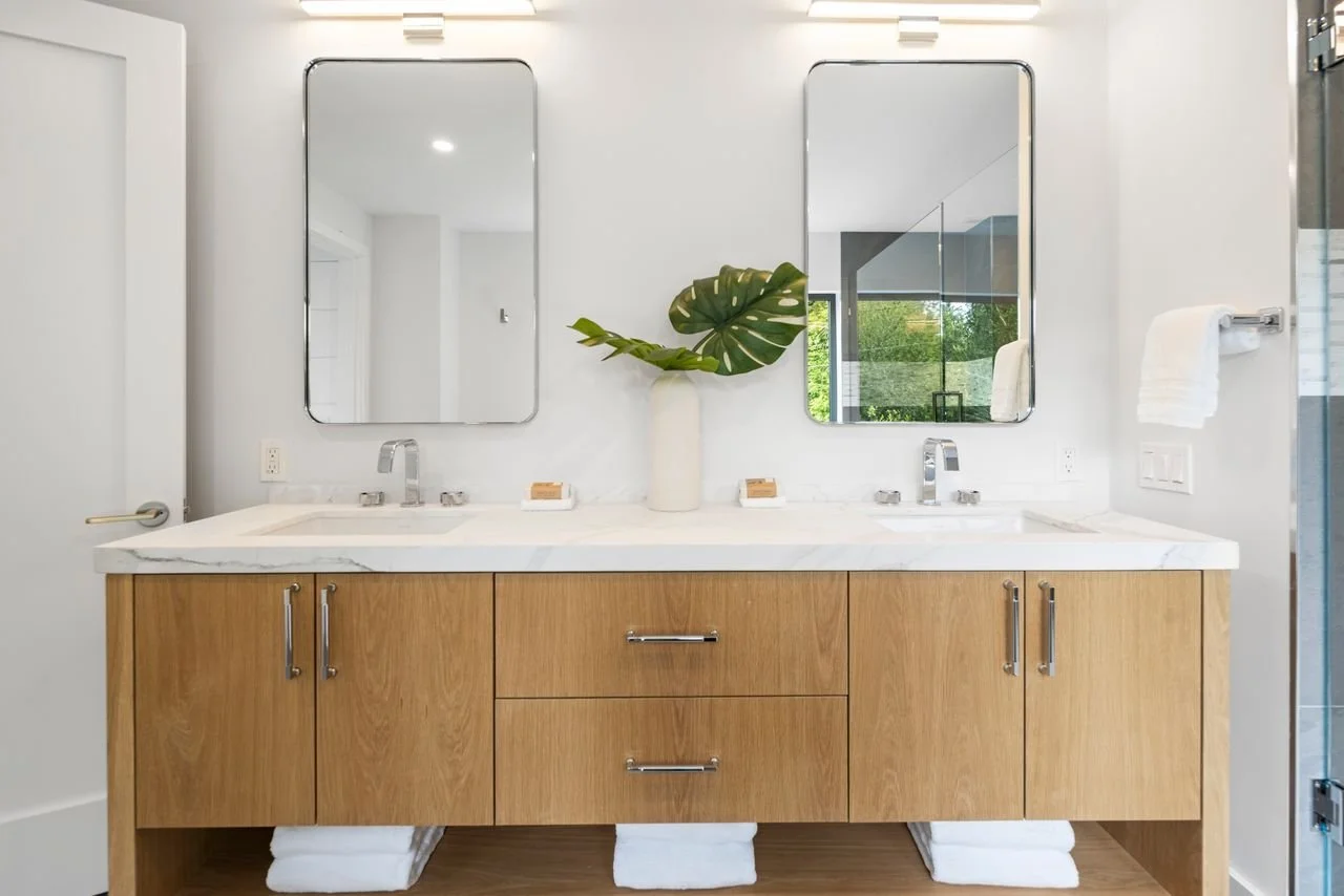 Modern bathroom vanity with a double sink, mirror cabinets, a large leaf in a white vase, and towels.