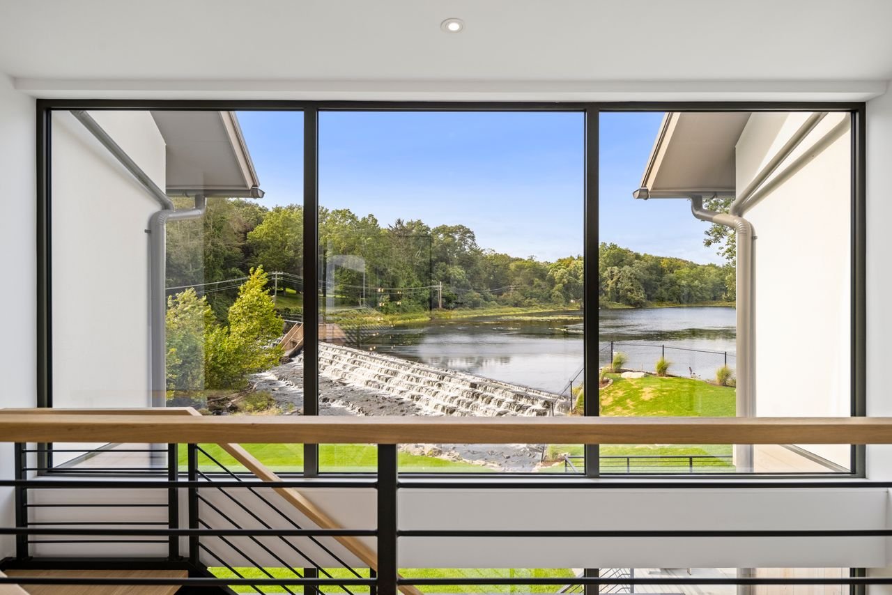 View of a river and park through a large glass window from inside a modern building.