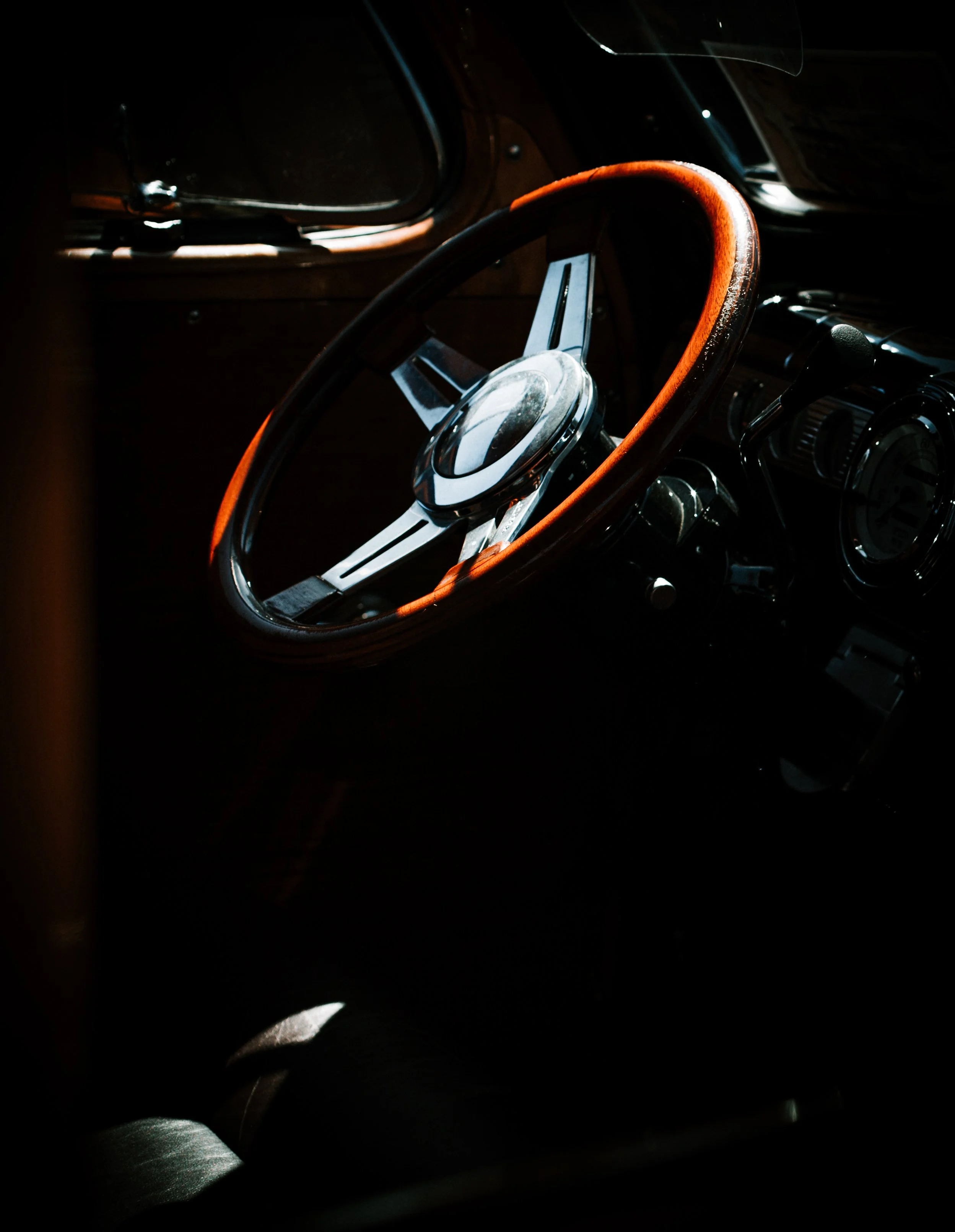 Close-up of a vintage car's interior, focusing on the steering wheel with a wooden rim and metal spokes.