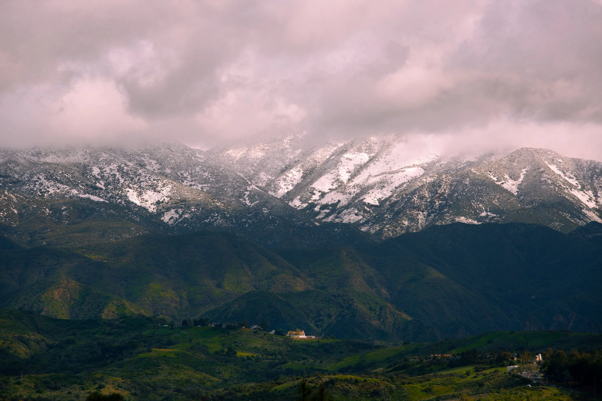 Cloud-covered snow-capped mountains over green rolling hills.