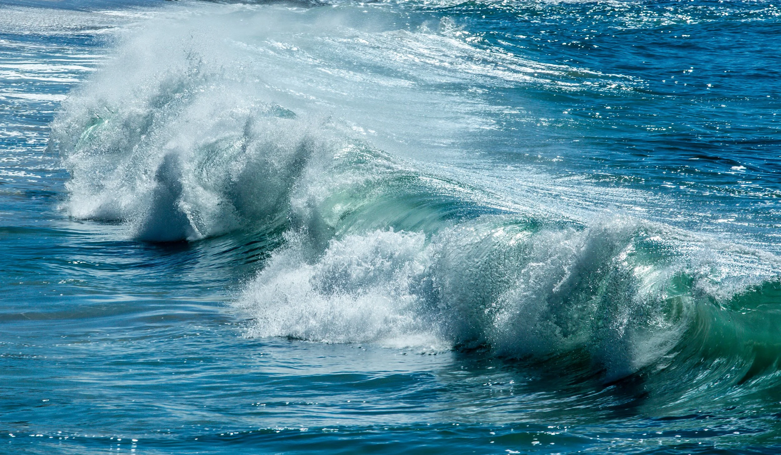 Ocean waves crashing with white foam and blue water under sunlight.