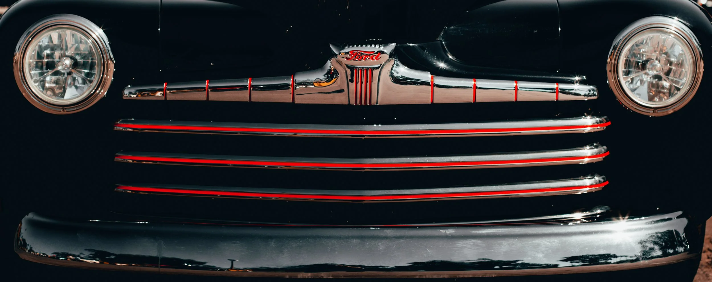 Close-up of a vintage black Ford car front with chrome grille, emblem, and round headlights
