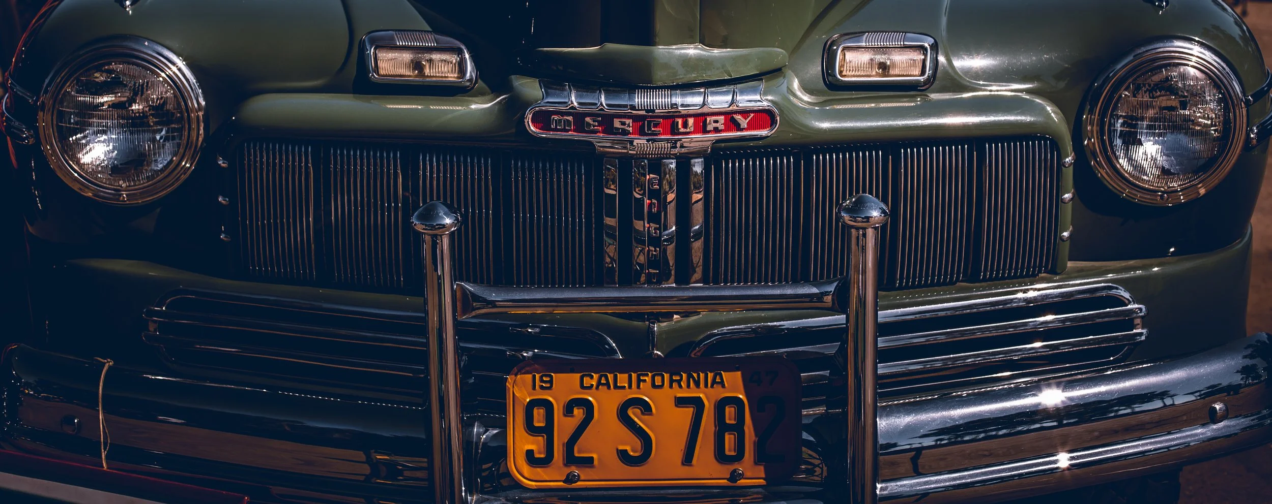 Close-up of the front of a vintage green Mercury car with chrome grille, round headlights, and California license plate reading 92 S 782.