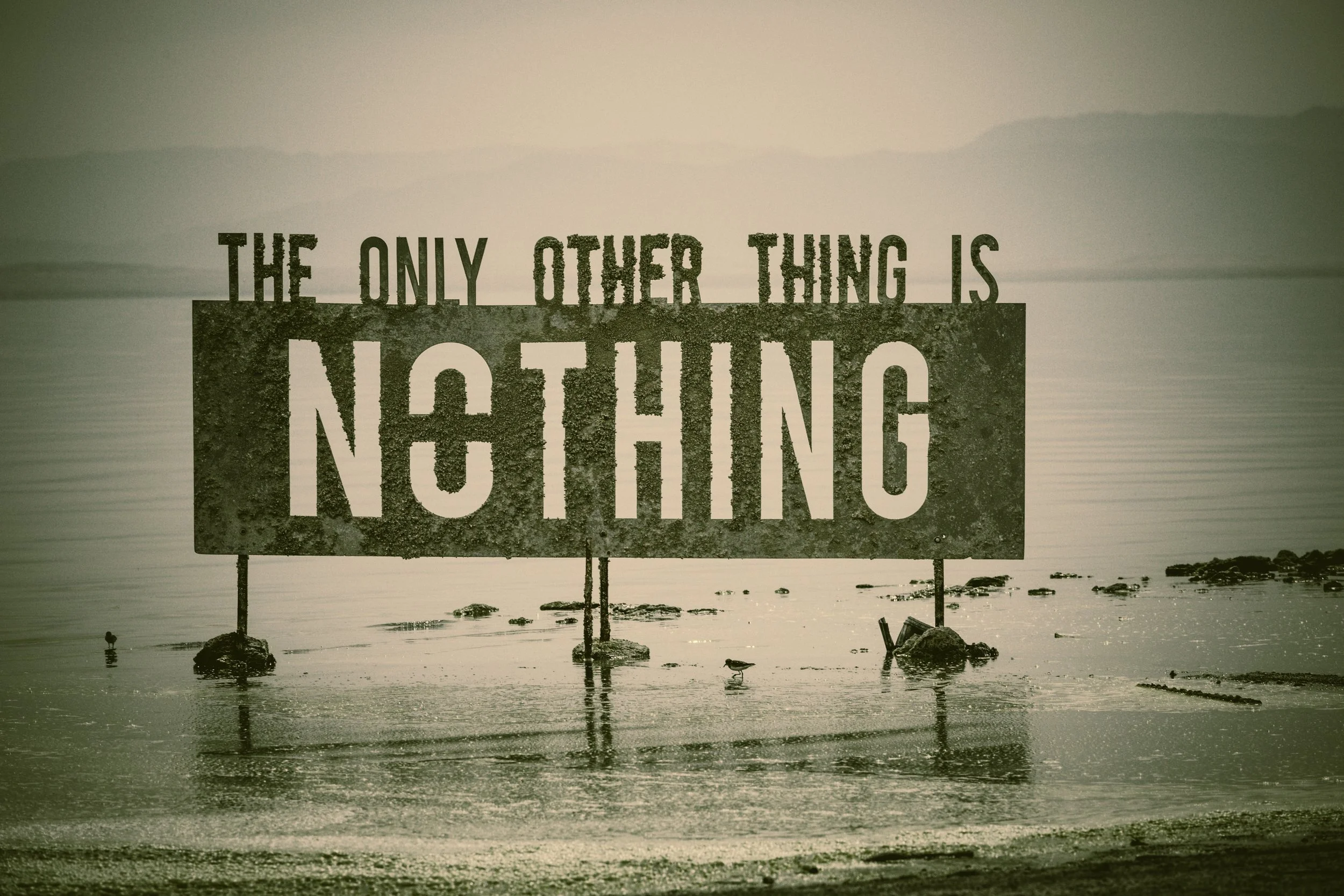 A large sign on a beach that reads 'The only other thing is nothing,' with the ocean and mountains in the background.