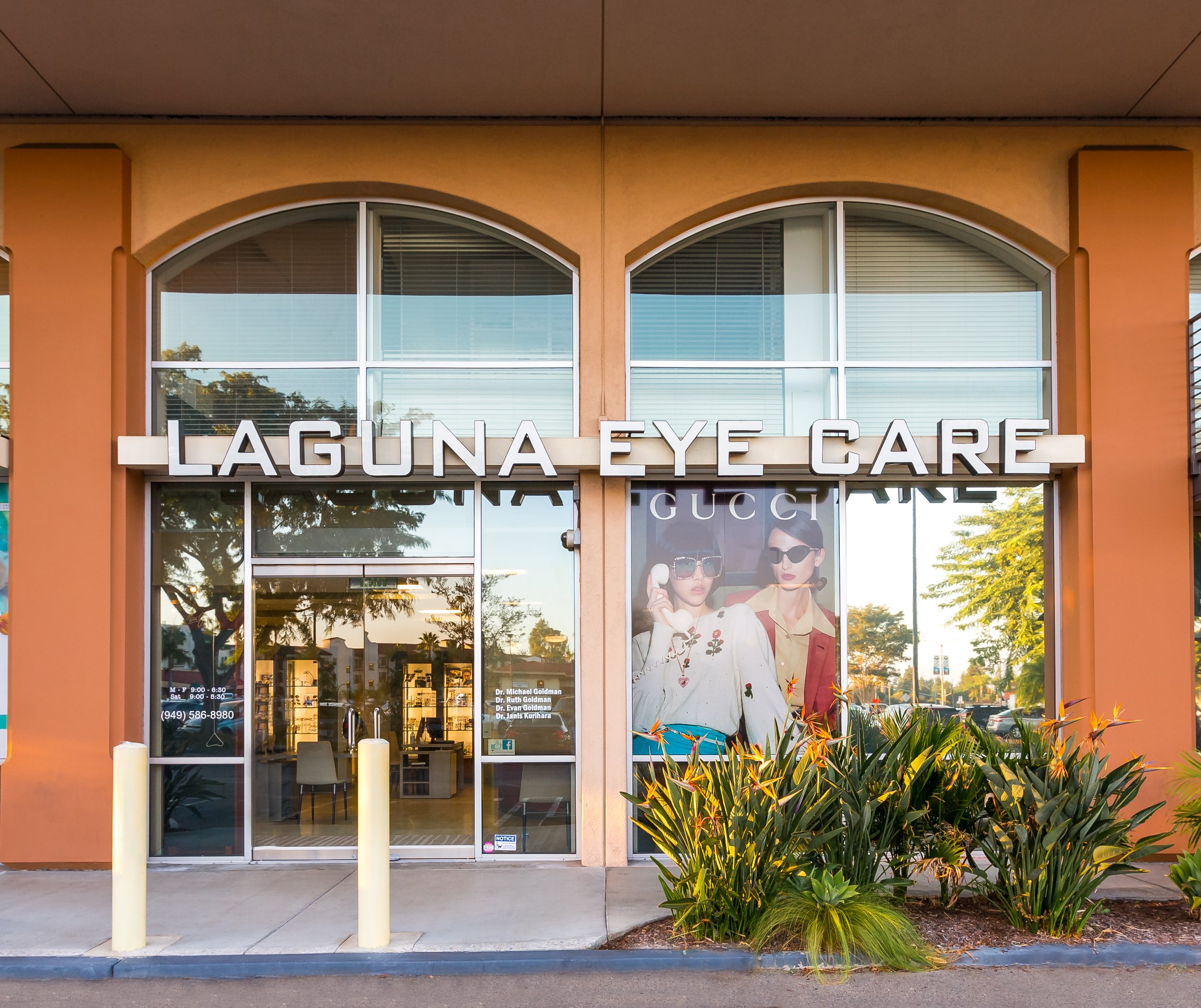 Storefront of Laguna Eye Care with large signage and window display featuring models wearing sunglasses, surrounded by green plants.