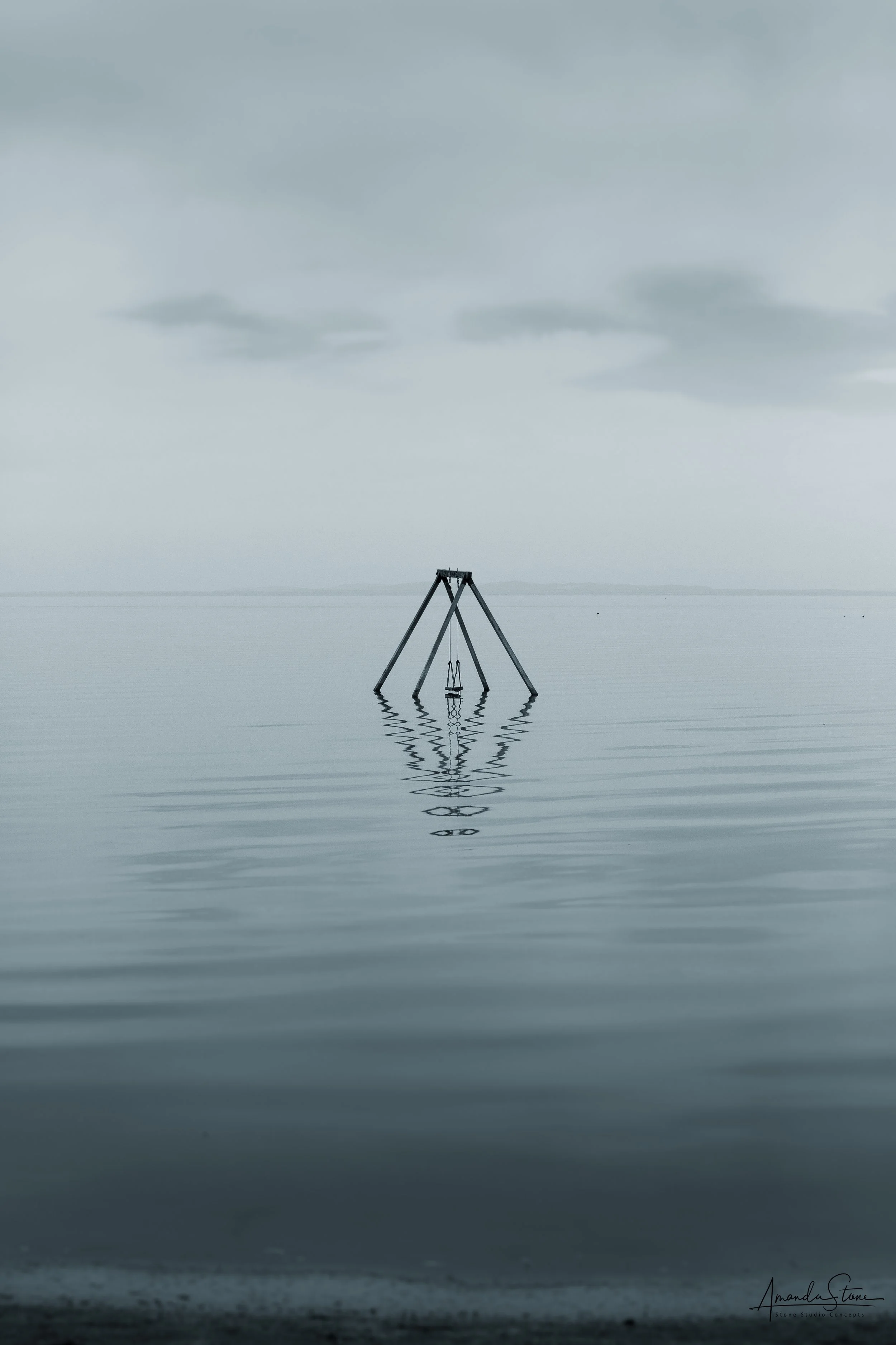 A swing set floating in a calm body of water, with its reflection visible in the water, under a cloudy sky.