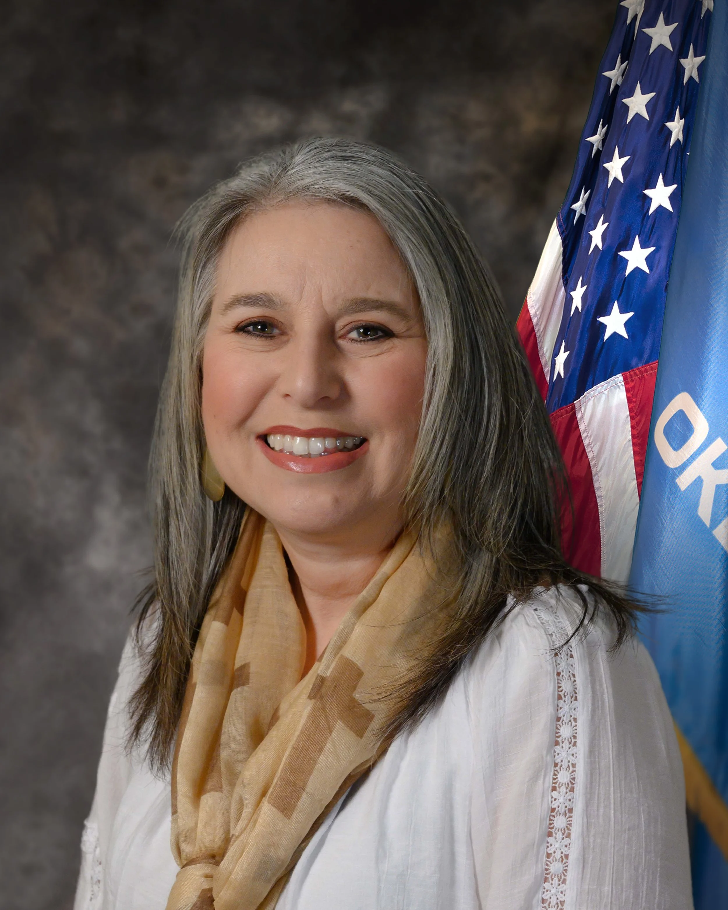 Headshot photo of Susie Suther, Davis City Manager, wearing a white top and neutral scarf positioned in front of an American Flag and State of Oklahoma Flag.