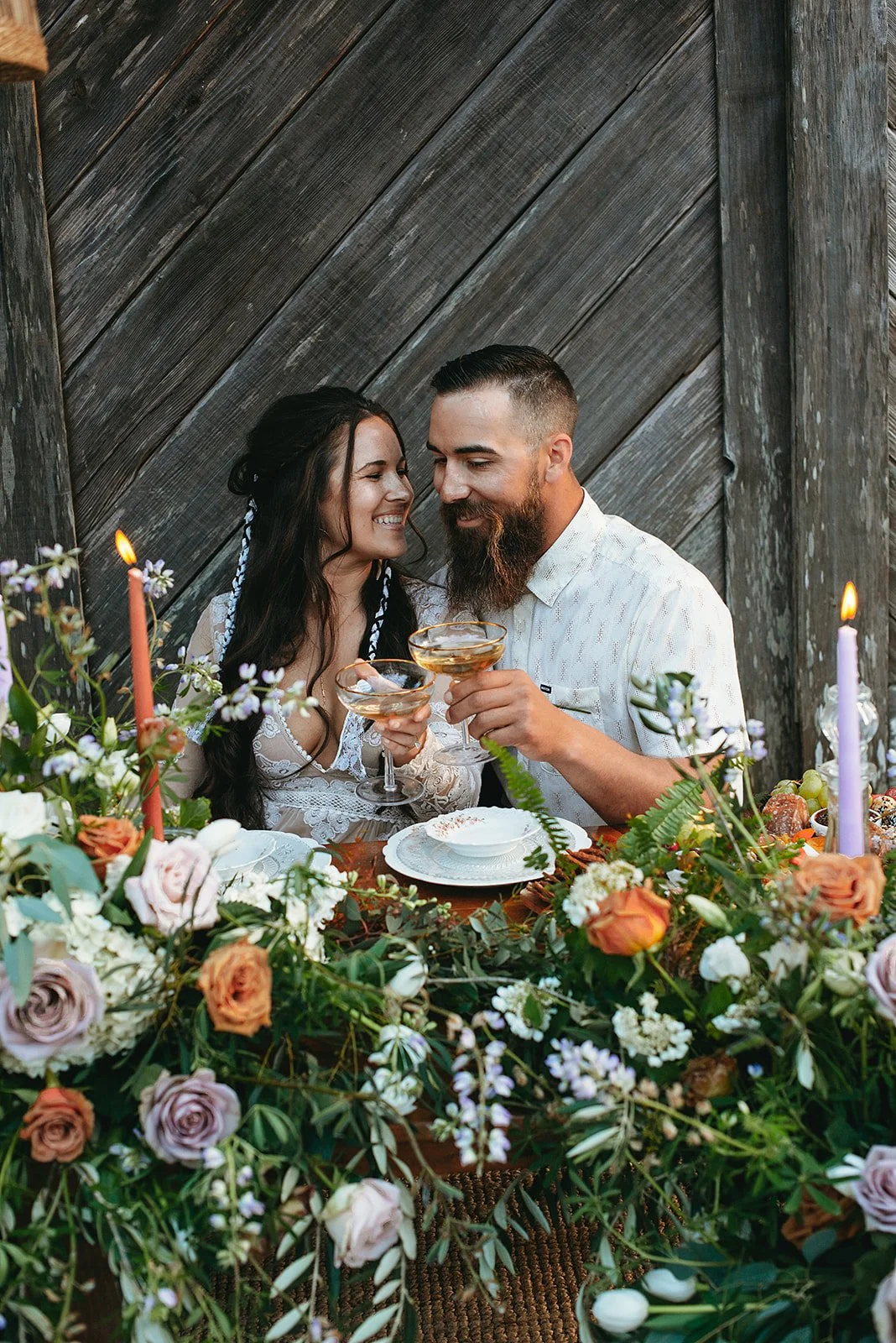 A couple celebrating at a dinner table decorated with flowers and candles, holding drinks and smiling at each other.