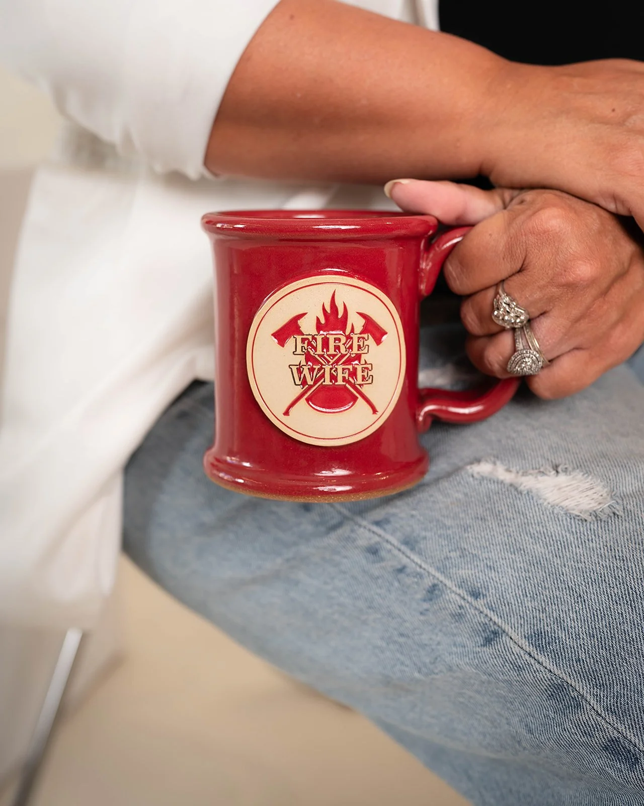 A person holding a red mug with a fire department emblem that reads 'Fire Wife' and features crossed axes and a flame design.