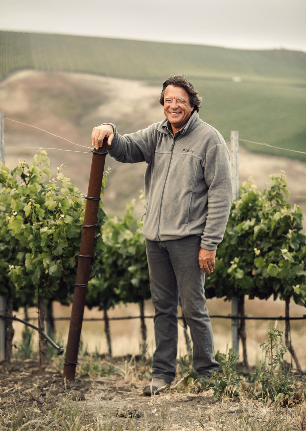 Mike with arm resting on vine trellis in a grey sweater and pants