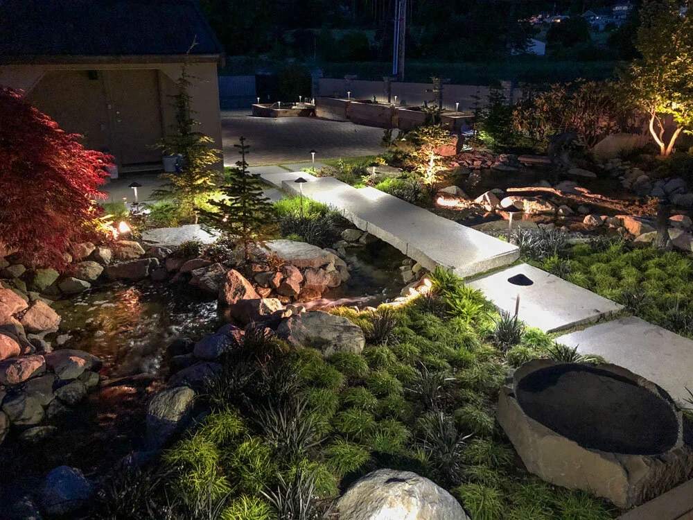 Illuminated stone bridge crossing a landscaped garden stream on Whidbey Island