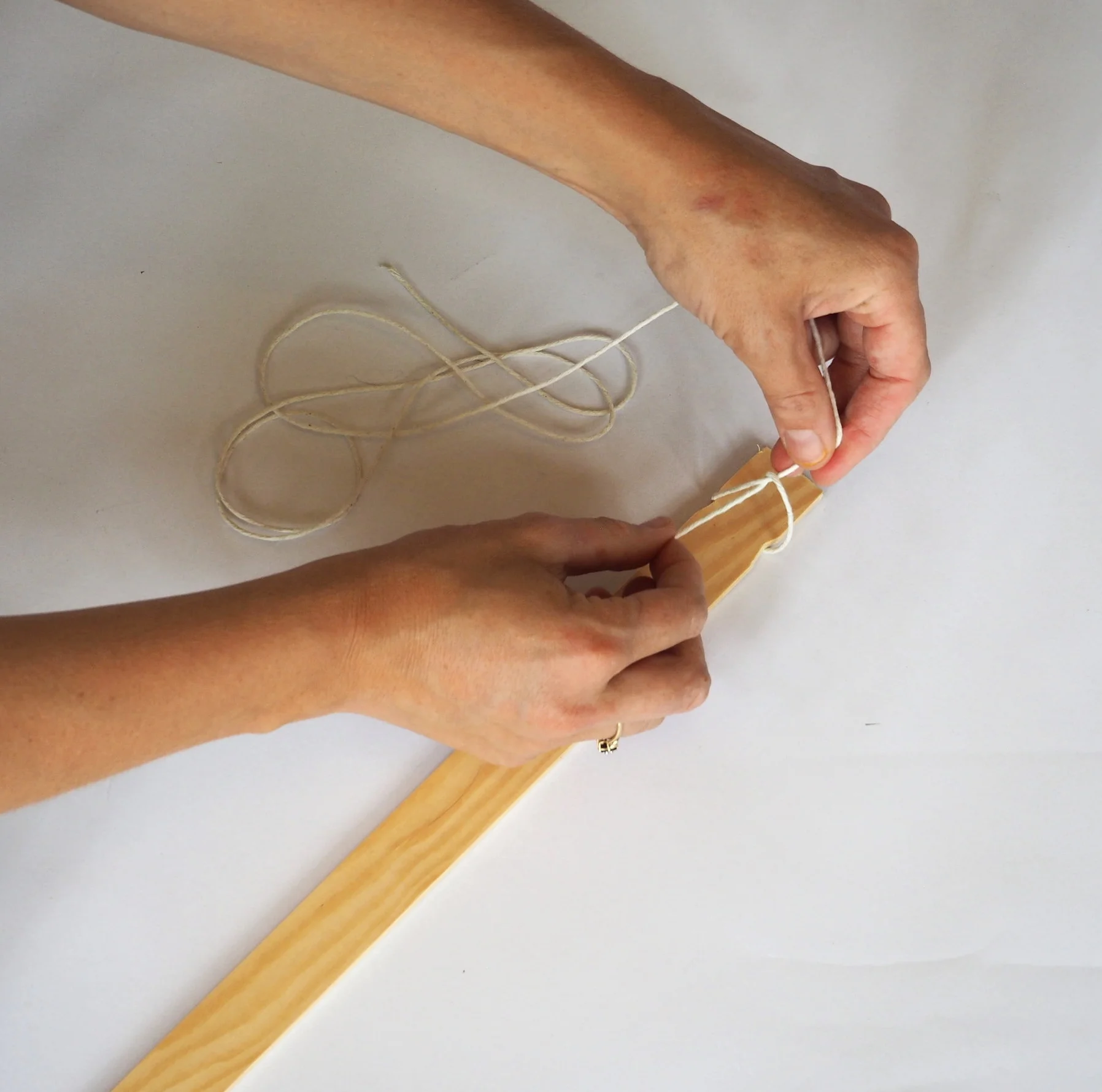  Take the last remaining piece of string (135cm) and tie it at one end of the long piece of wood. 