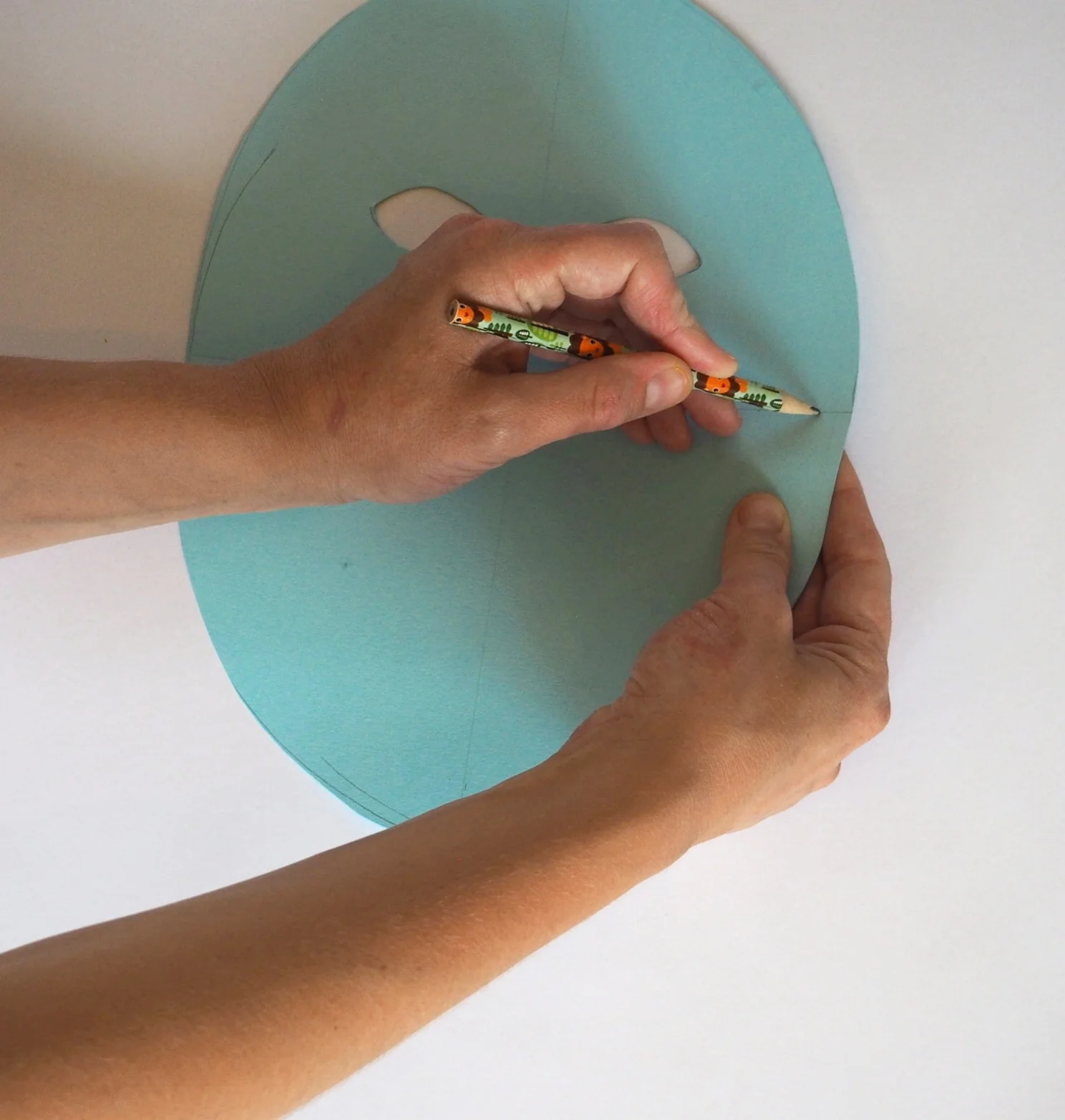  Carefully push your pencil through the card about 1cm from edge of mask, making a hole for the elastic to thread through later. You might want to hold it up to your face first, to measure where to make the hole. Again, get an adult to help you with 