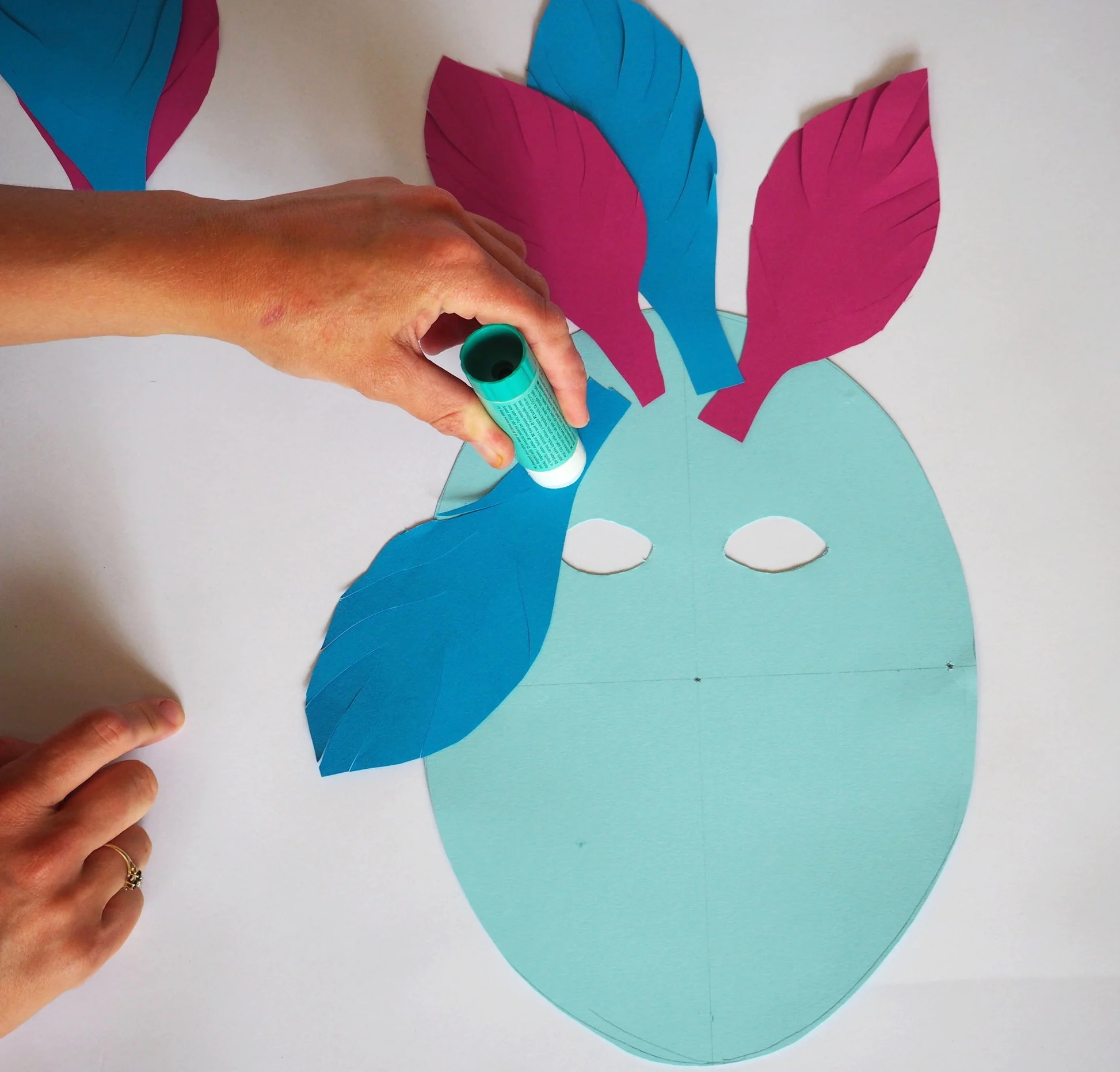  Using your glue stick the feather shapes on the the back of your mask (the side with the pencil lines). 