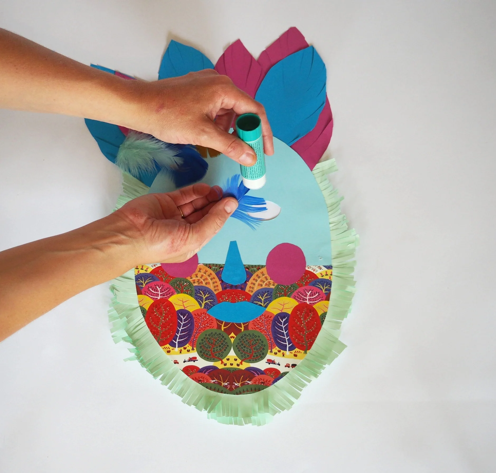  Apply glue to the top of each of your feathers and stick them just below your paper feathers on the front of your mask. 