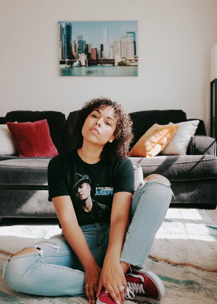 woman sitting on floor in a living room wearing worn jeans and a justin timberlake tshirt