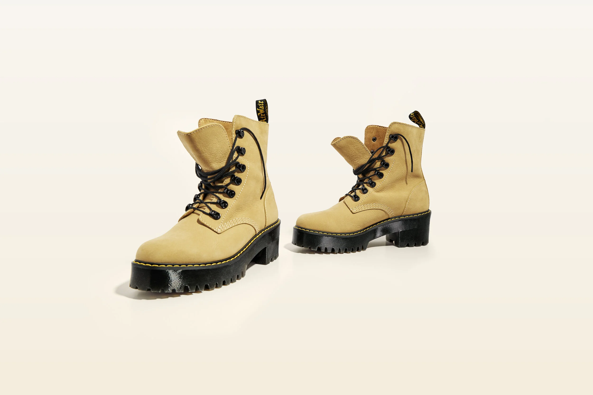 Pair of beige leather boots with black chunky soles and black laces, on a plain white background.