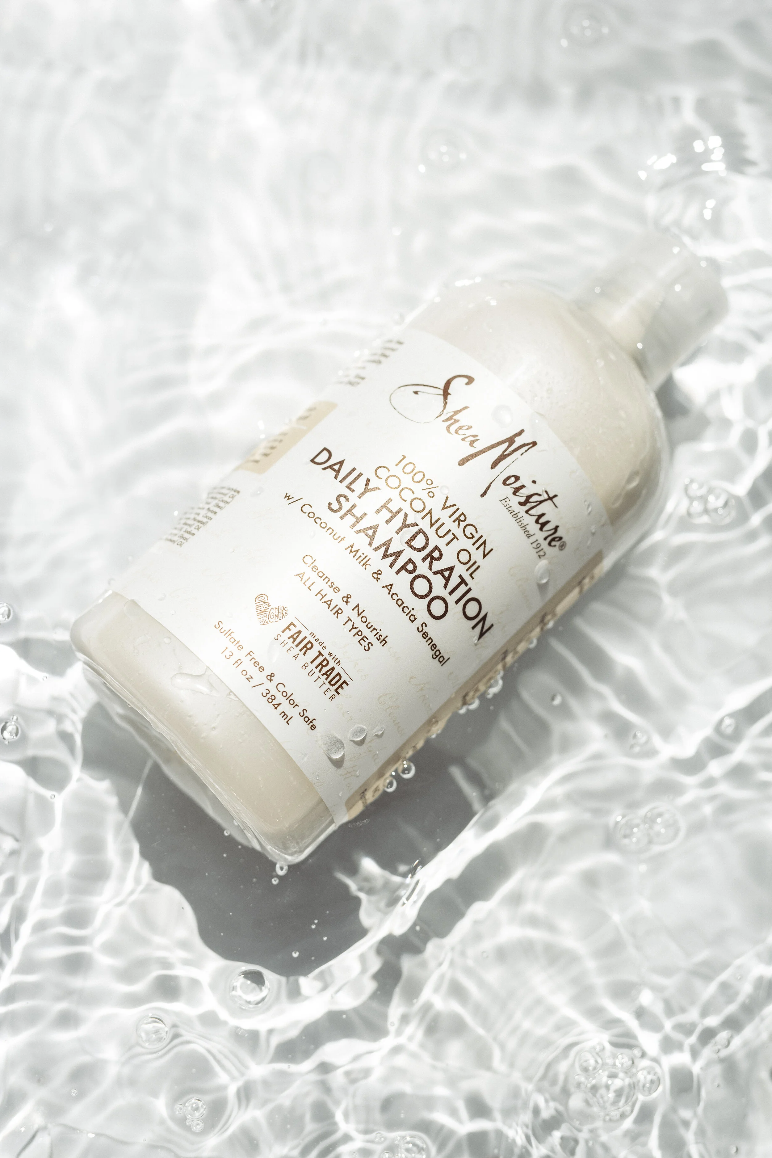 A bottle of SheaMoisture daily hydrating shampoo lying on water with ripples, bubbles, and reflections.