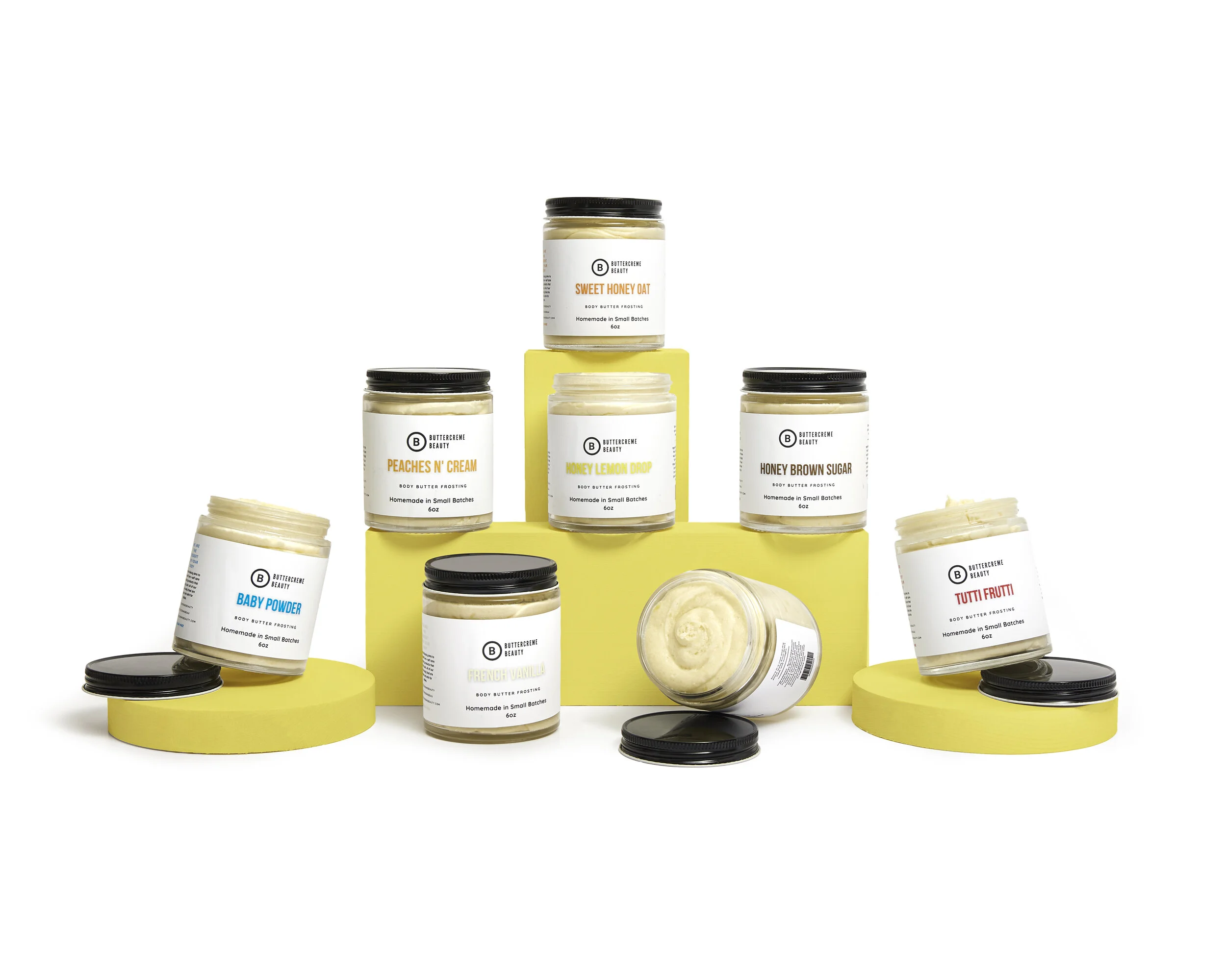 Collection of body butter frosting jars in various flavors on yellow platforms.