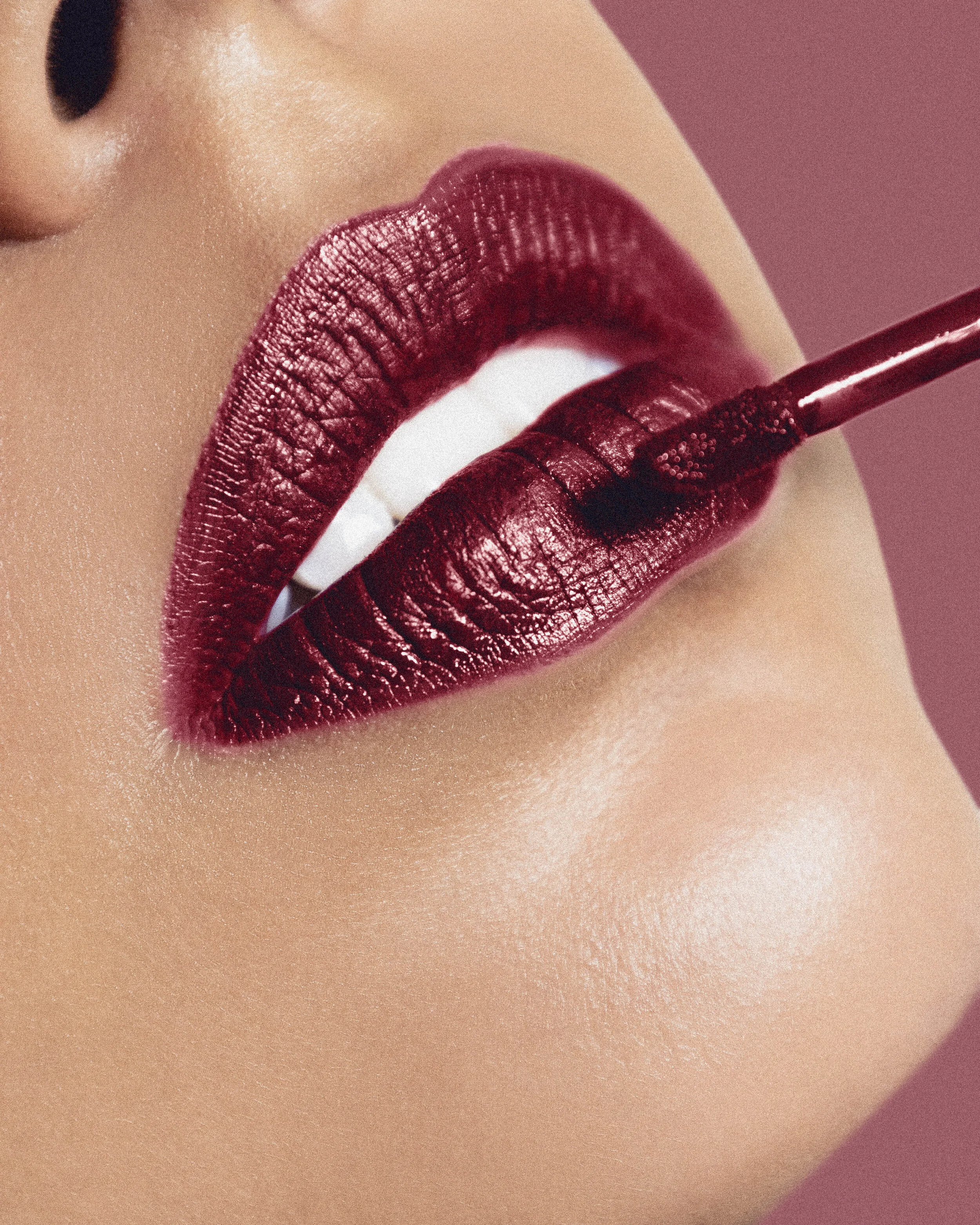 Close-up of a woman applying dark red lipstick from a gloss tube, with her lips slightly parted.