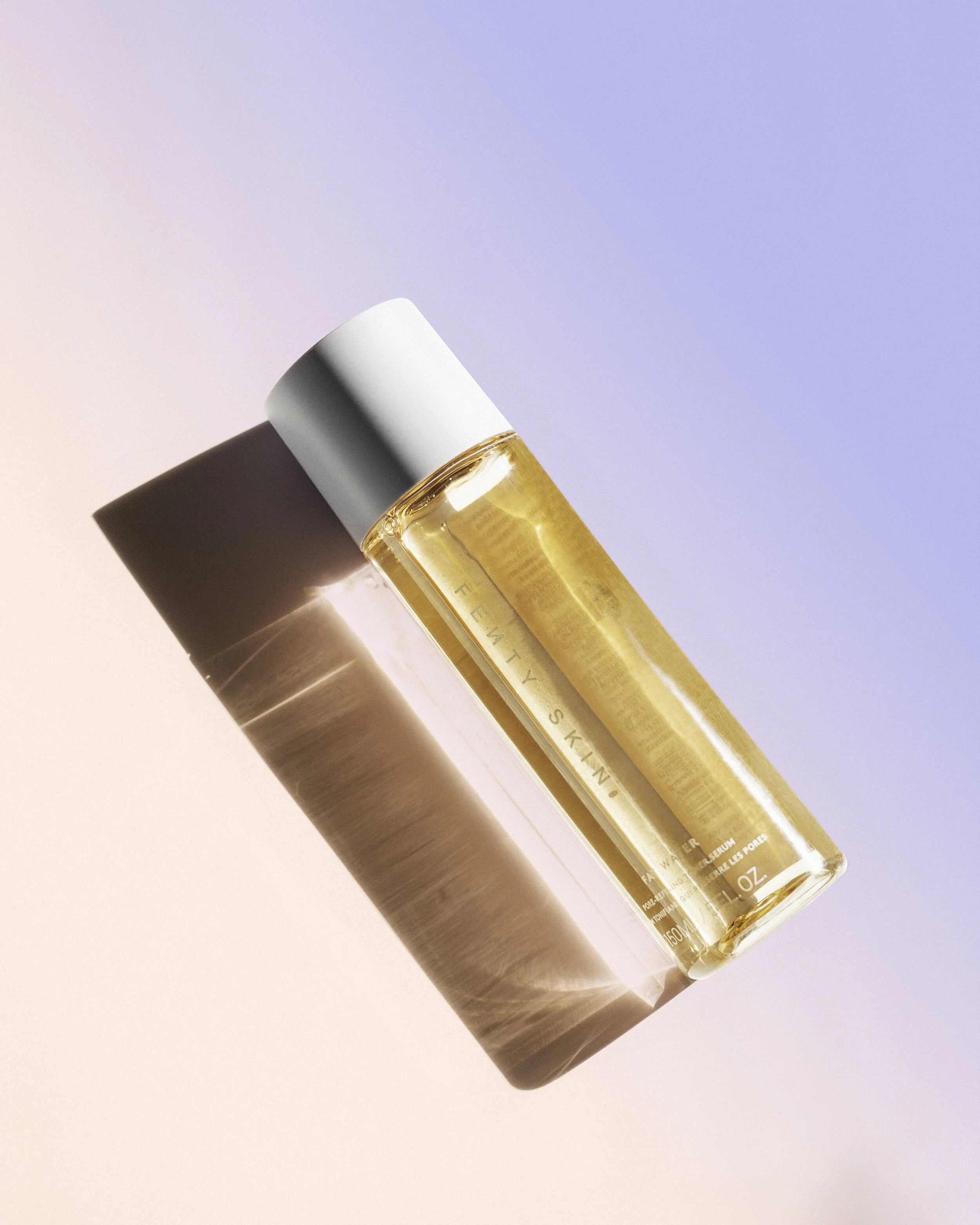 A clear bottle of skincare serum with a white cap, casting a shadow on a pastel-colored background.