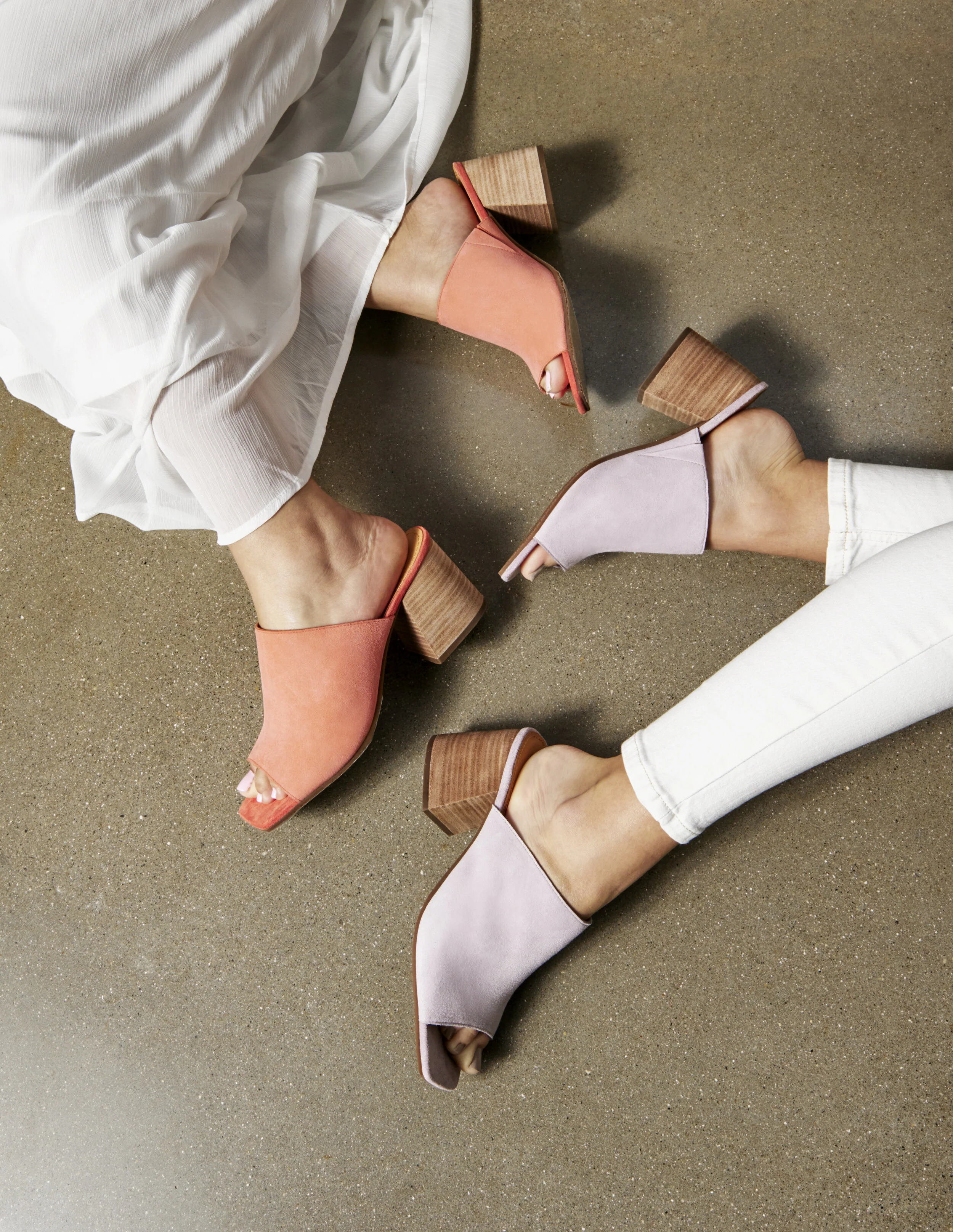 Two people wearing pastel-colored open-toe high heel shoes lying on a speckled brown floor.