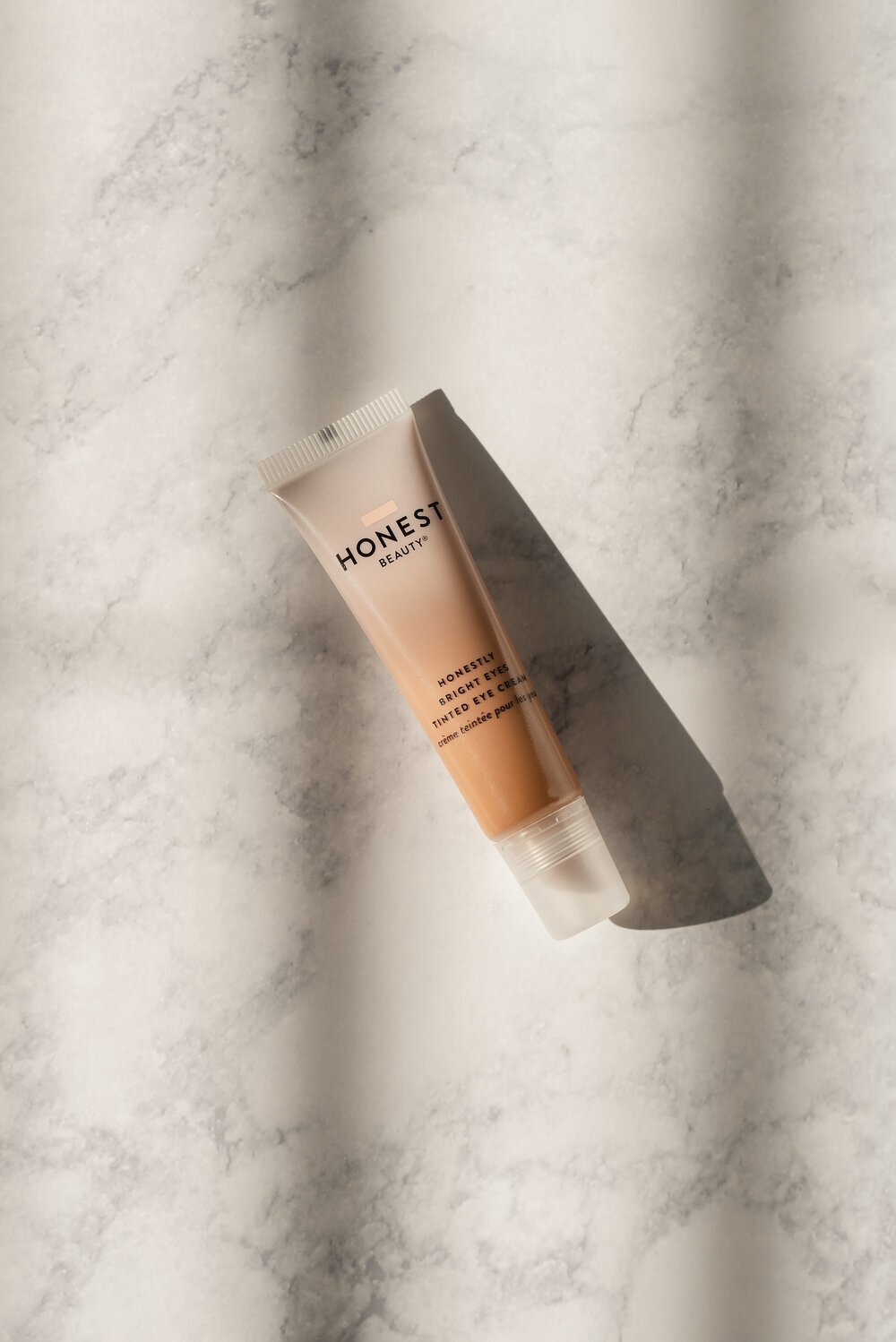 Tube of Honest Beauty Bright Eyes Tinted Eye Cream on marble surface with shadow cast to the right.