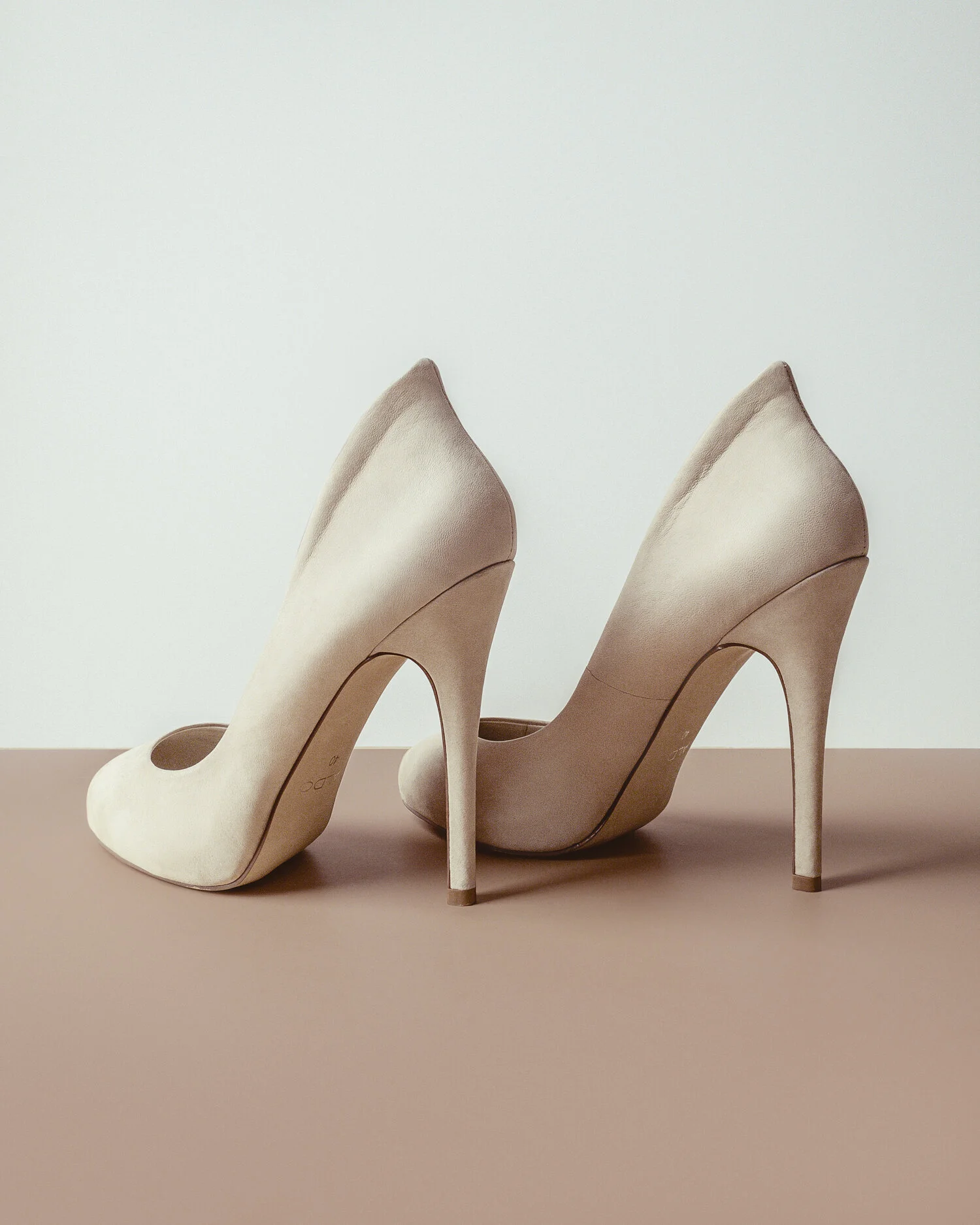 A pair of beige high-heeled shoes placed on a flat surface against a white background.