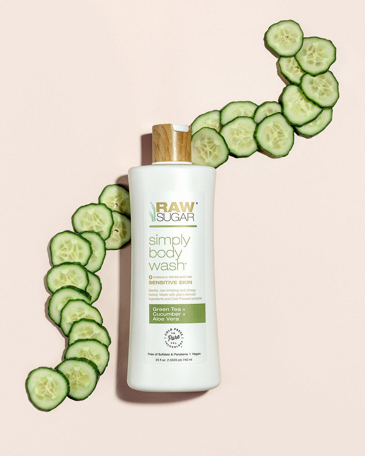 A bottle of RAW Sugar Simply Body Wash with cucumber and aloe, surrounded by sliced cucumbers, on a light pink background.